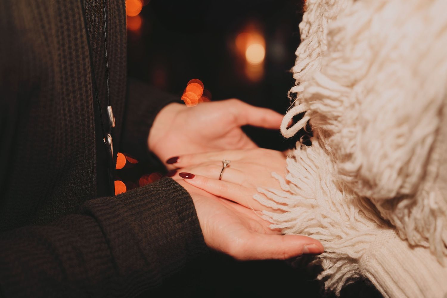 Close-up of marriage proposal ring being placed on womans finger with bokeh lights.