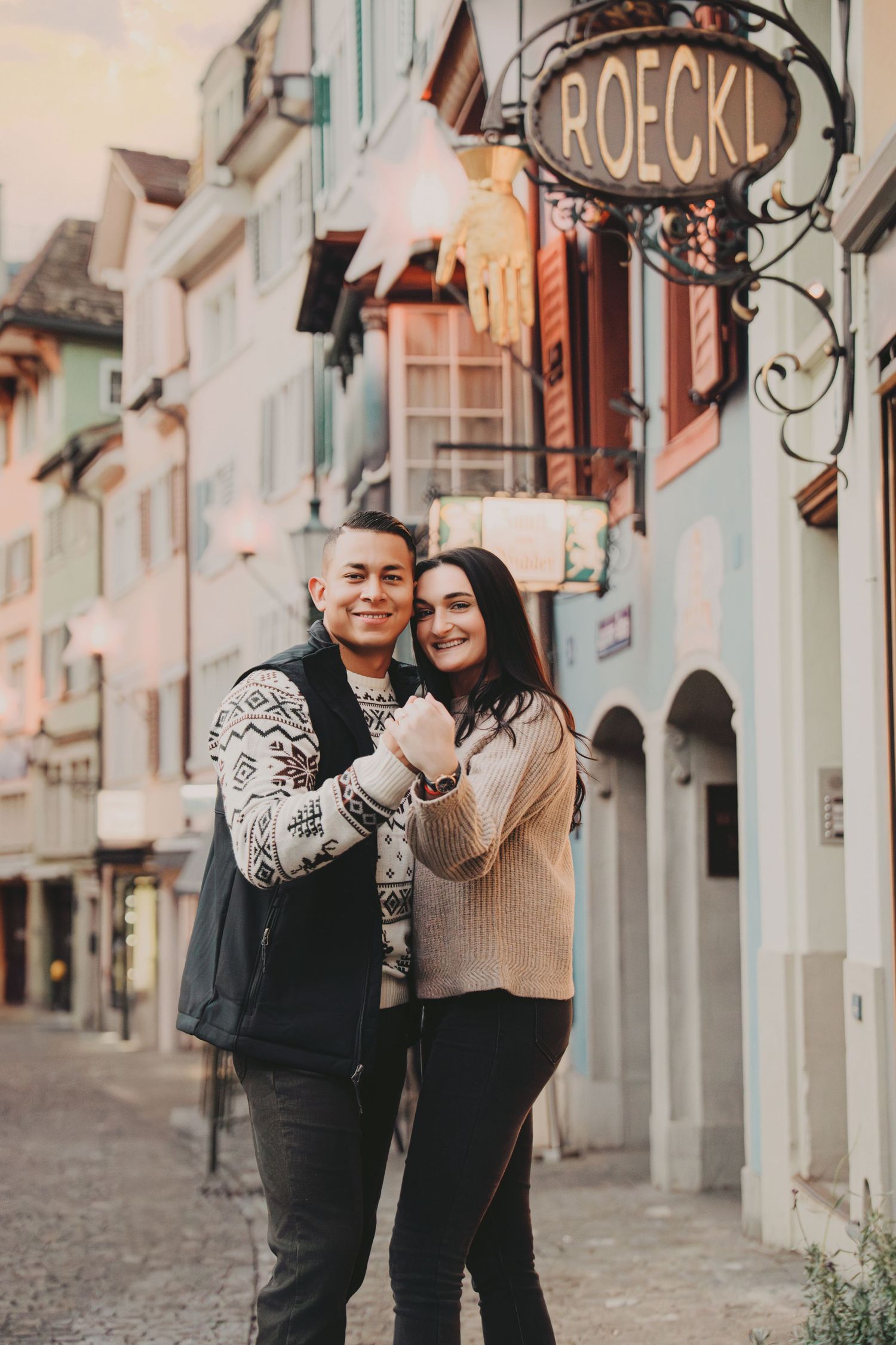 Smiling couple posing together on a charming old town street in Zurich near the Roeckl sign.