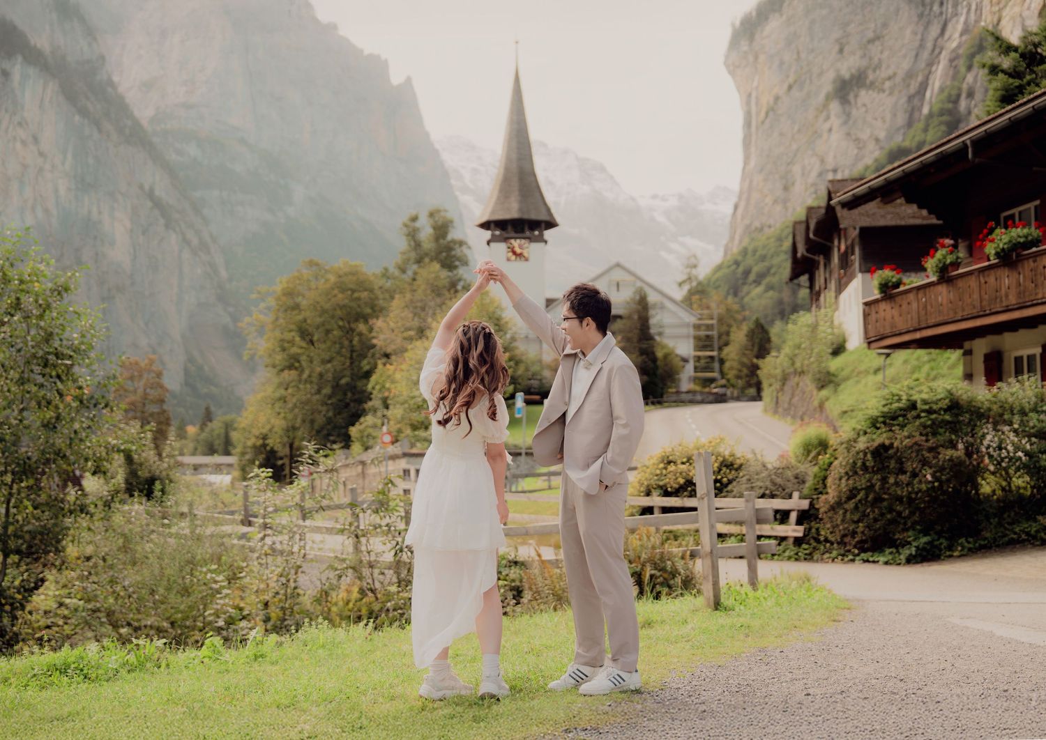 Couple twirling together on a scenic Swiss village path with a church steeple backdrop.