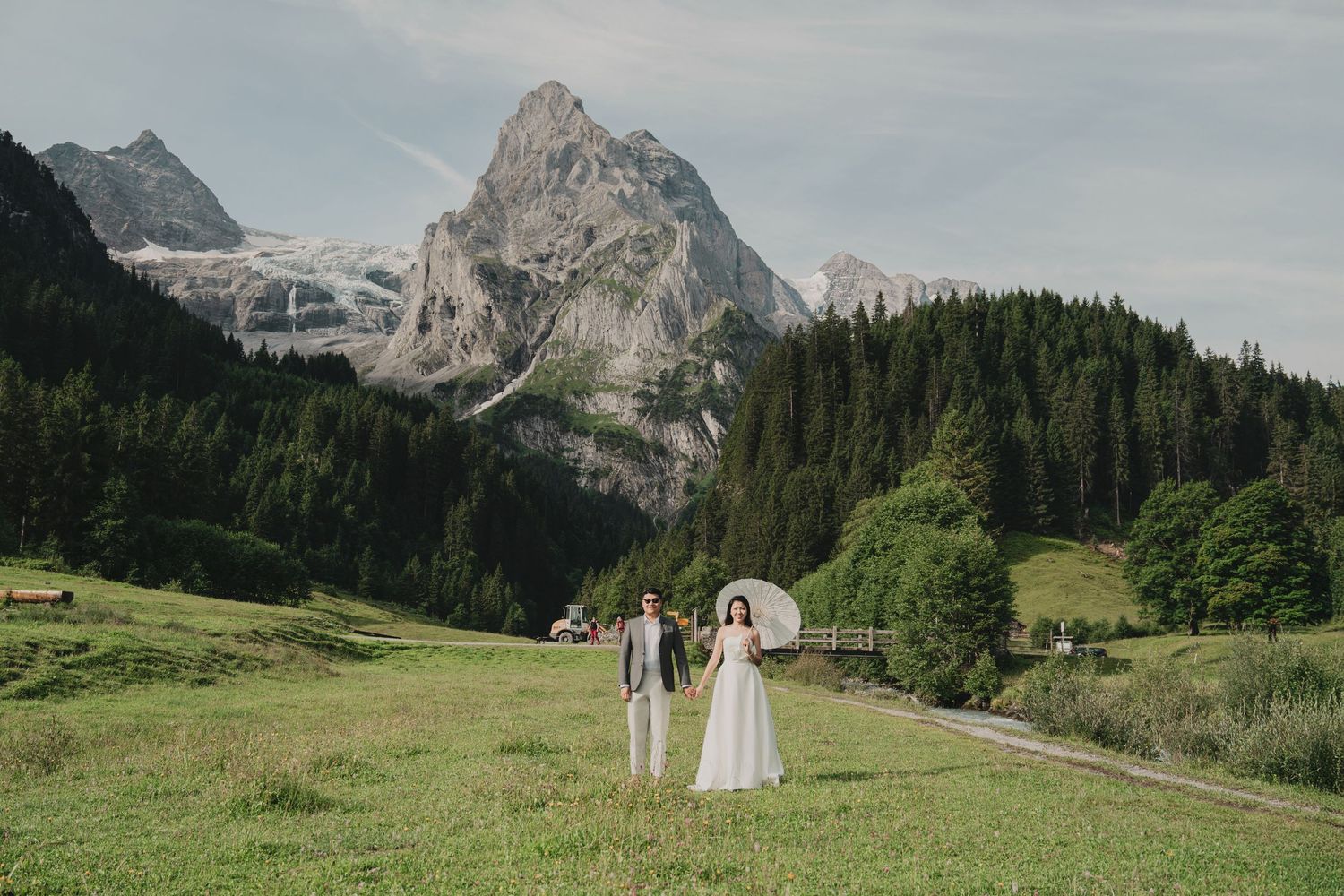 Couple holding hands in alpine meadow with dramatic mountain peaks and glacier backdrop on their wedding day.