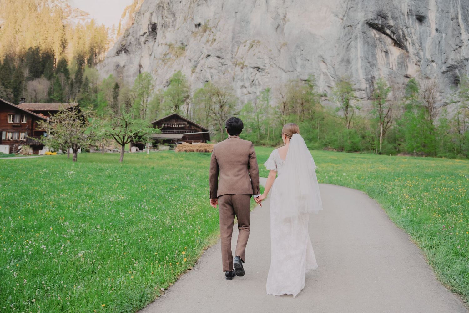 Bride and groom walk hand in hand away from camera on a path through a stunning Swiss alpine landscape.