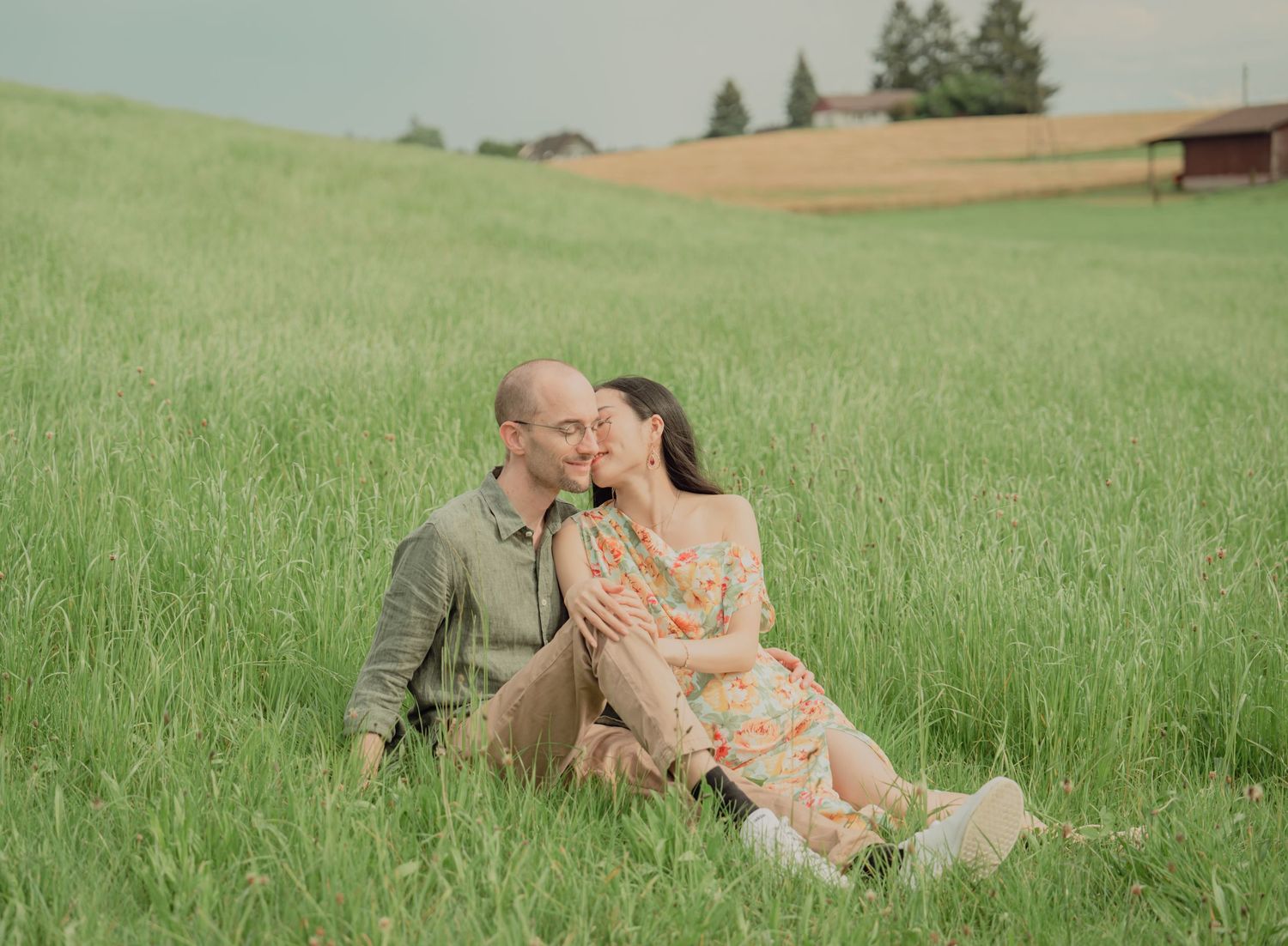 Happy couple sitting together in a lush green meadow, sharing a tender romantic moment outdoors.