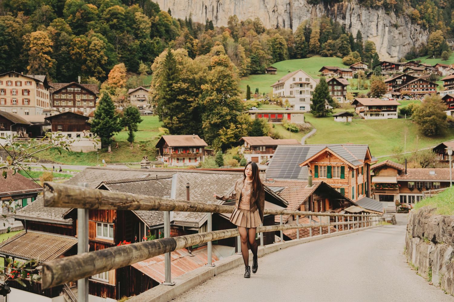 Woman posing on a bridge overlooking a charming Swiss mountain village with wooden chalets.