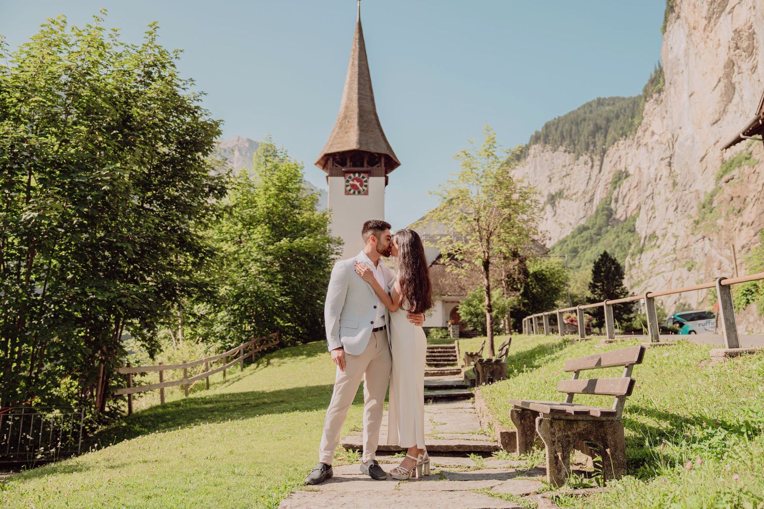Couple kissing near a historic church tower in a scenic Swiss mountain village.