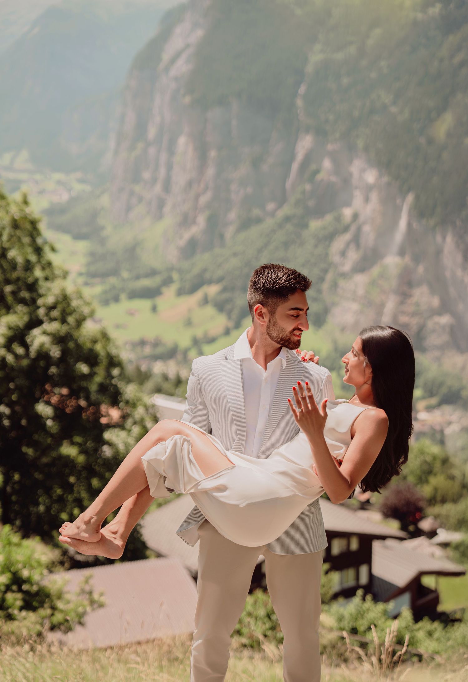 Groom carrying bride in his arms with stunning Swiss mountain valley backdrop on wedding day.