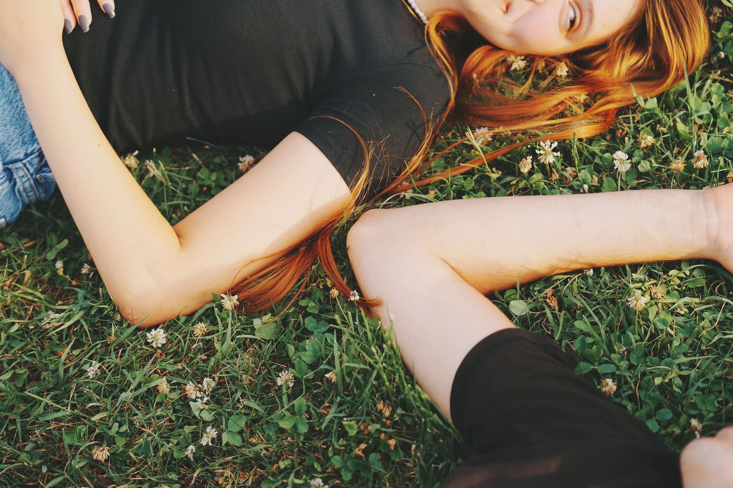 Couple lying together on green clover-filled grass, woman with vibrant red hair relaxing.