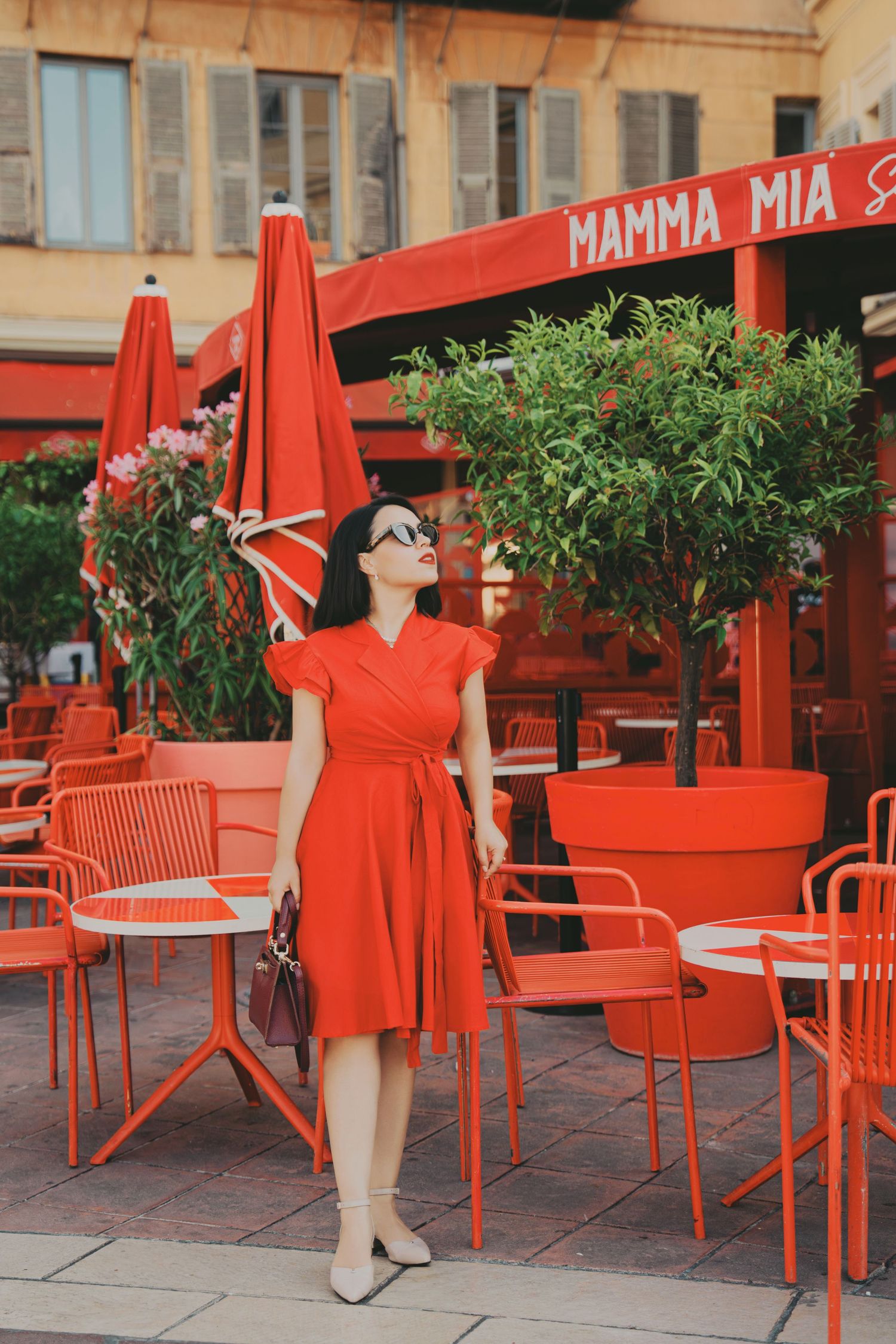 Woman in red wrap dress standing outside Mamma Mia cafe with red outdoor seating.