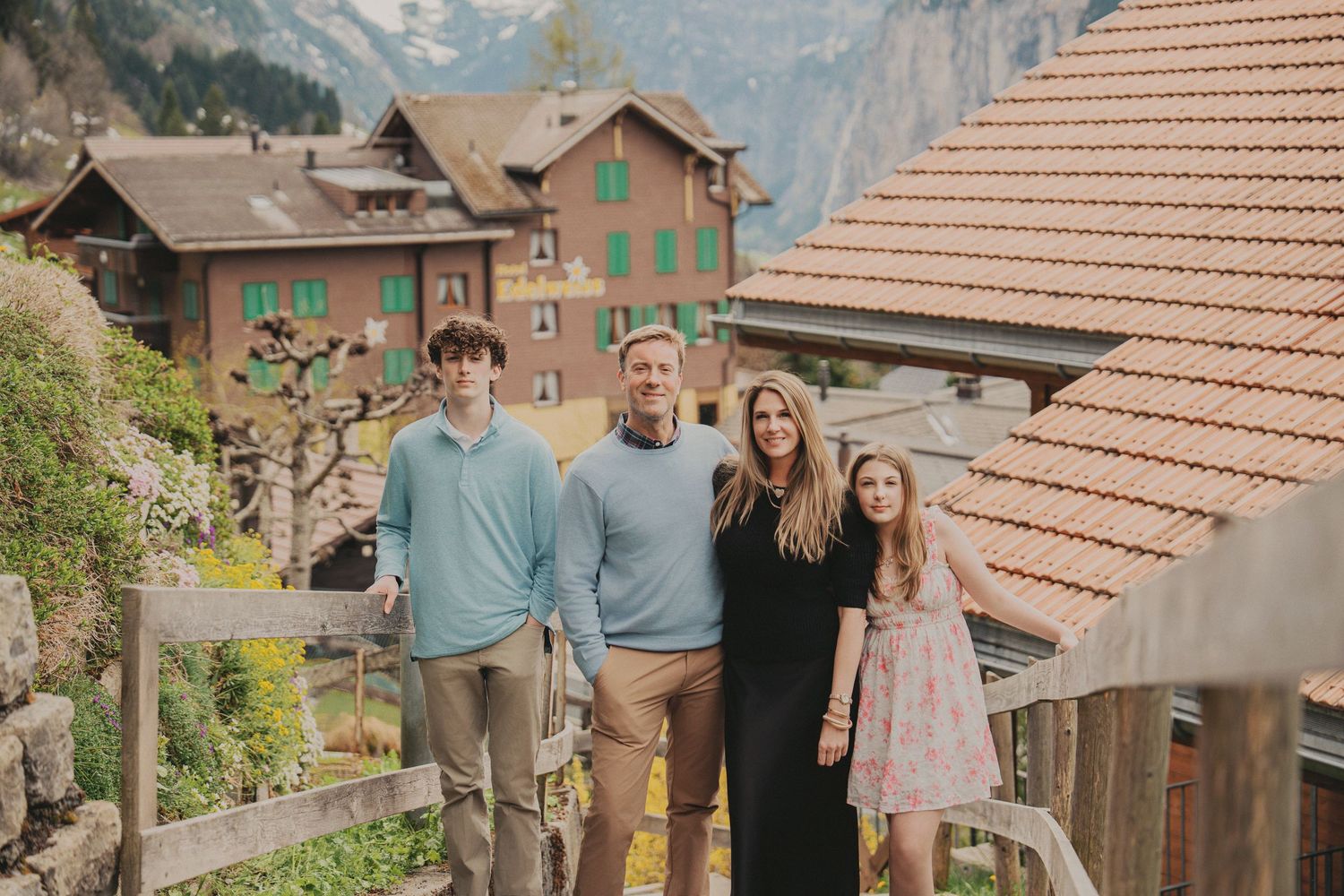 Family of four smiling together in a charming Swiss village with traditional buildings behind them.