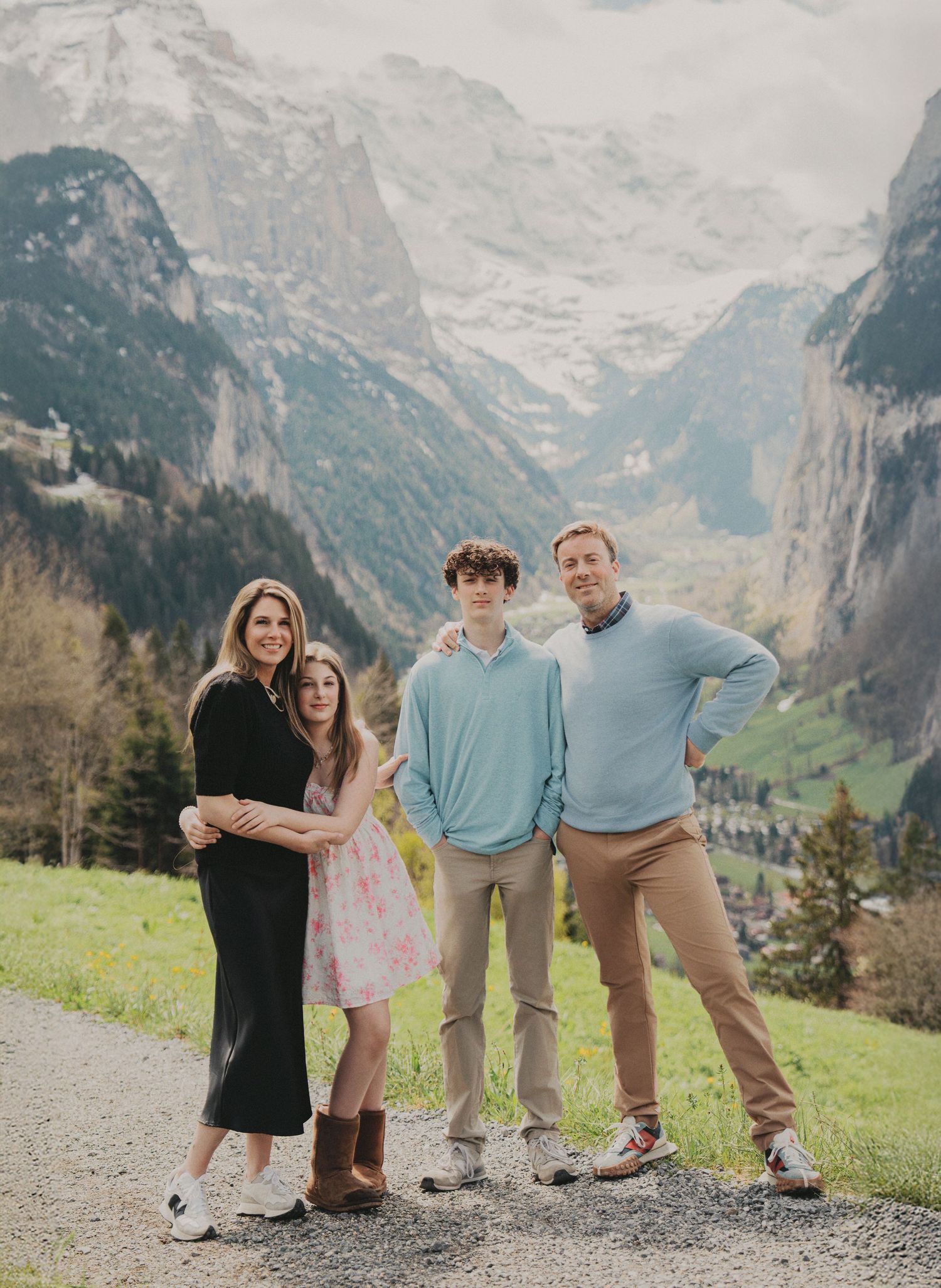 Family of four stands on gravel path with stunning Swiss Alps mountain valley backdrop in spring.