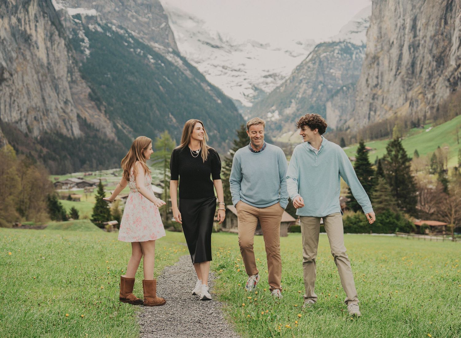Smiling family walking together on a scenic path through a lush green Swiss alpine valley landscape.
