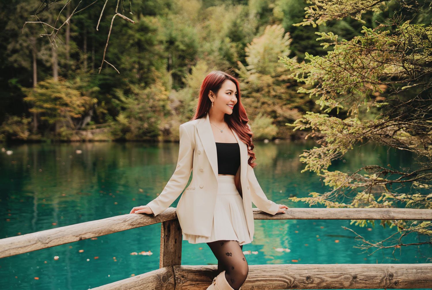 Beautiful woman in white blazer and black top posing by stunning turquoise mountain lake.
