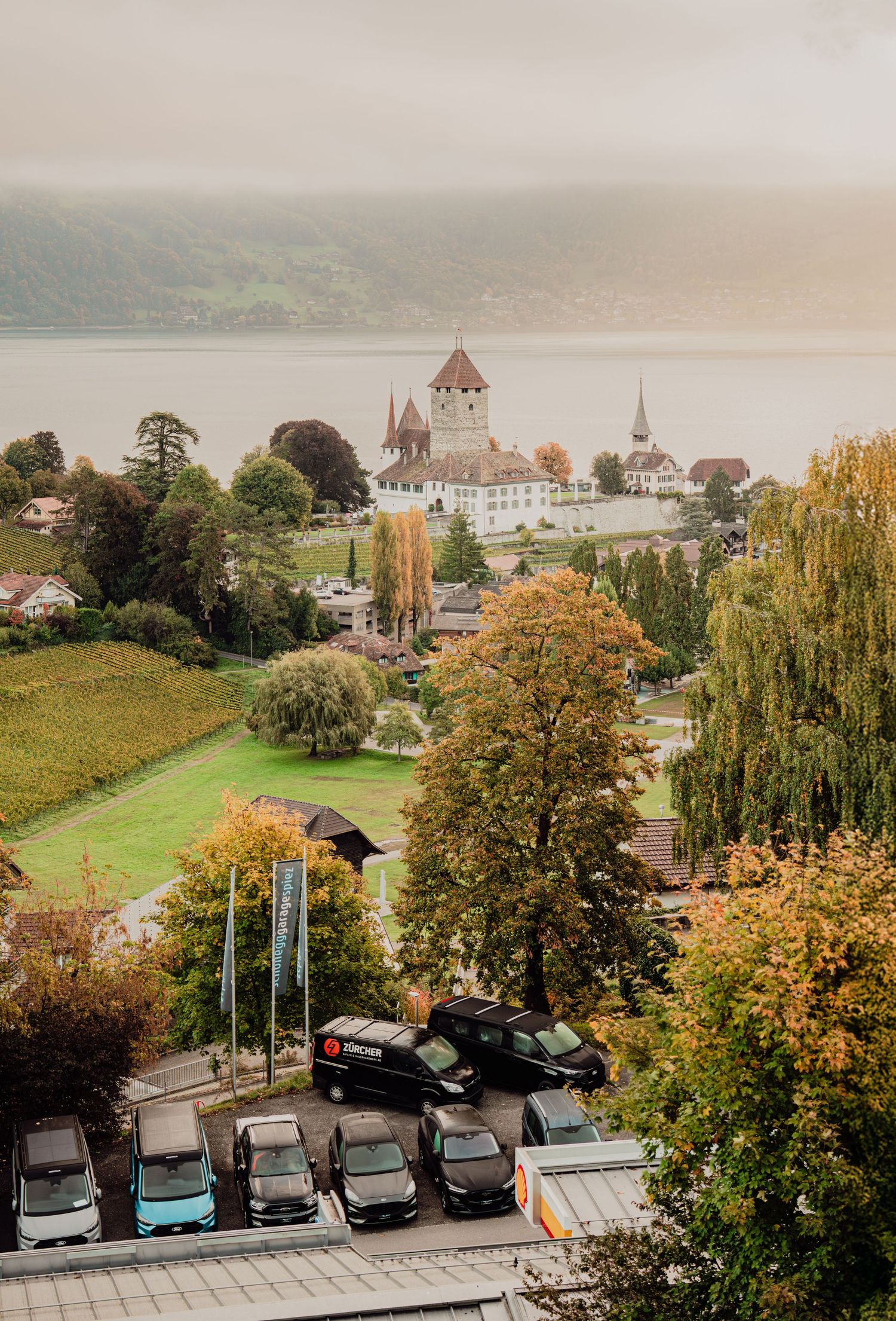 Aerial autumn view of Spiez Castle and Lake Thun in Switzerland with a parking lot in foreground.