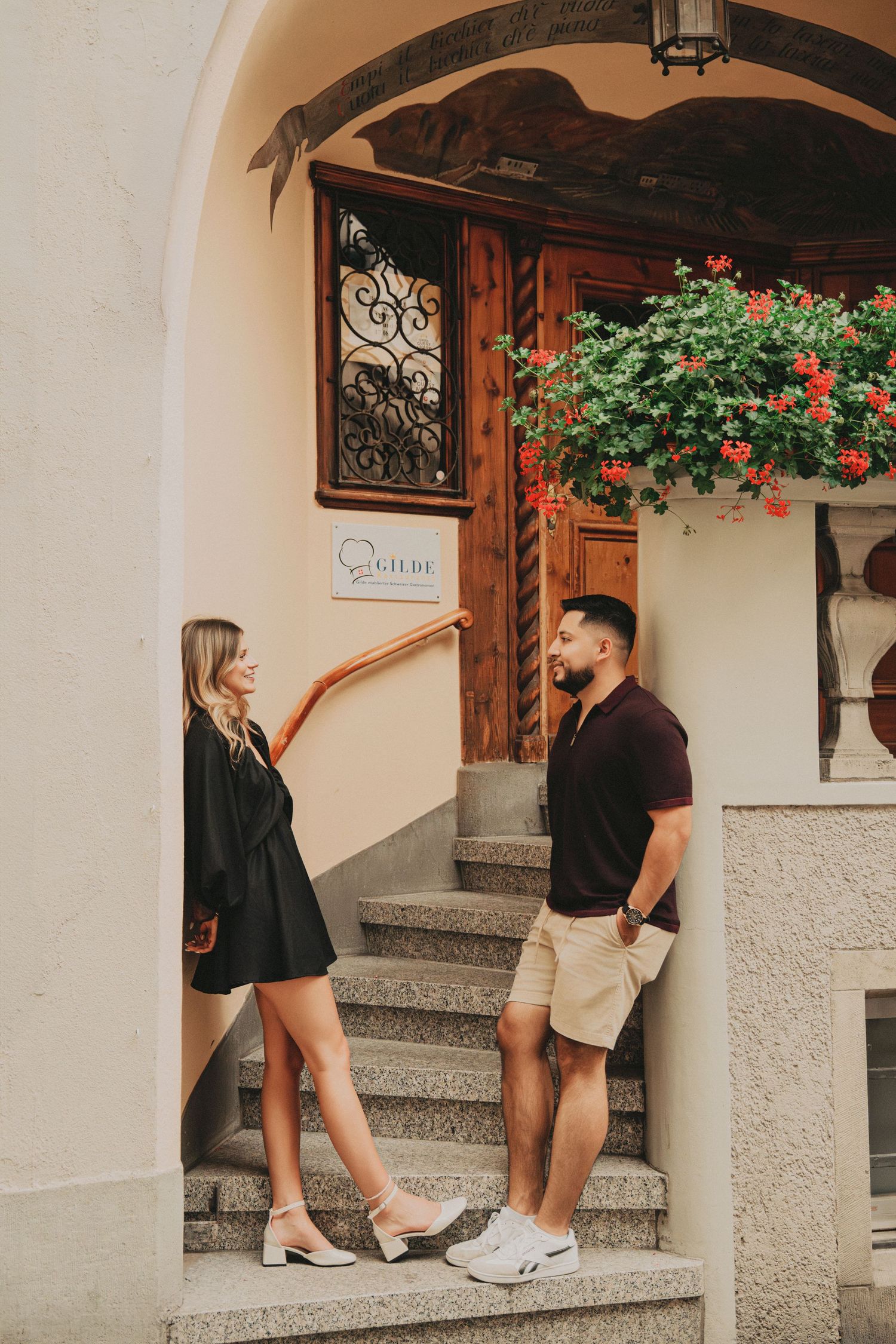 Couple chatting on stone steps of a historic Zurich building with red flowers.