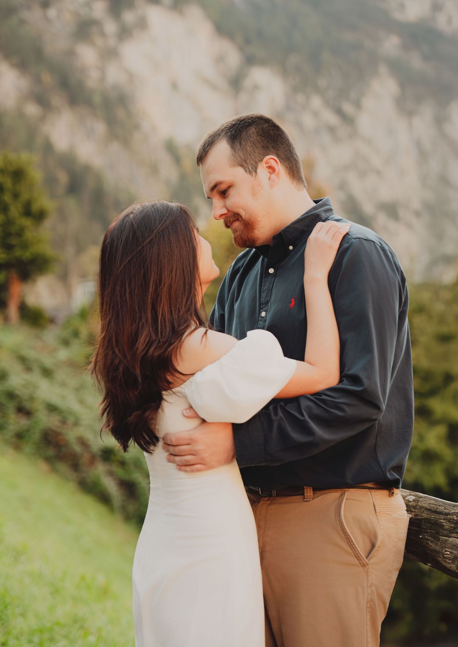 Couple embracing and smiling at each other with mountain scenery in background.