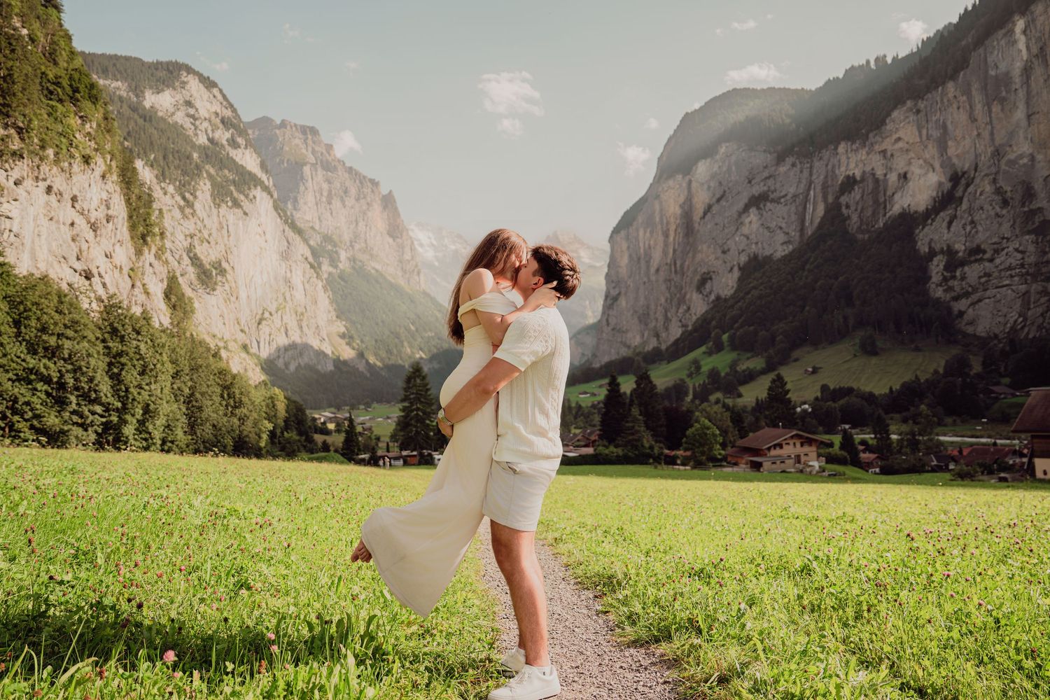 Couple kissing in a lush green meadow with dramatic Swiss Alps cliffs in Lauterbrunnen valley.