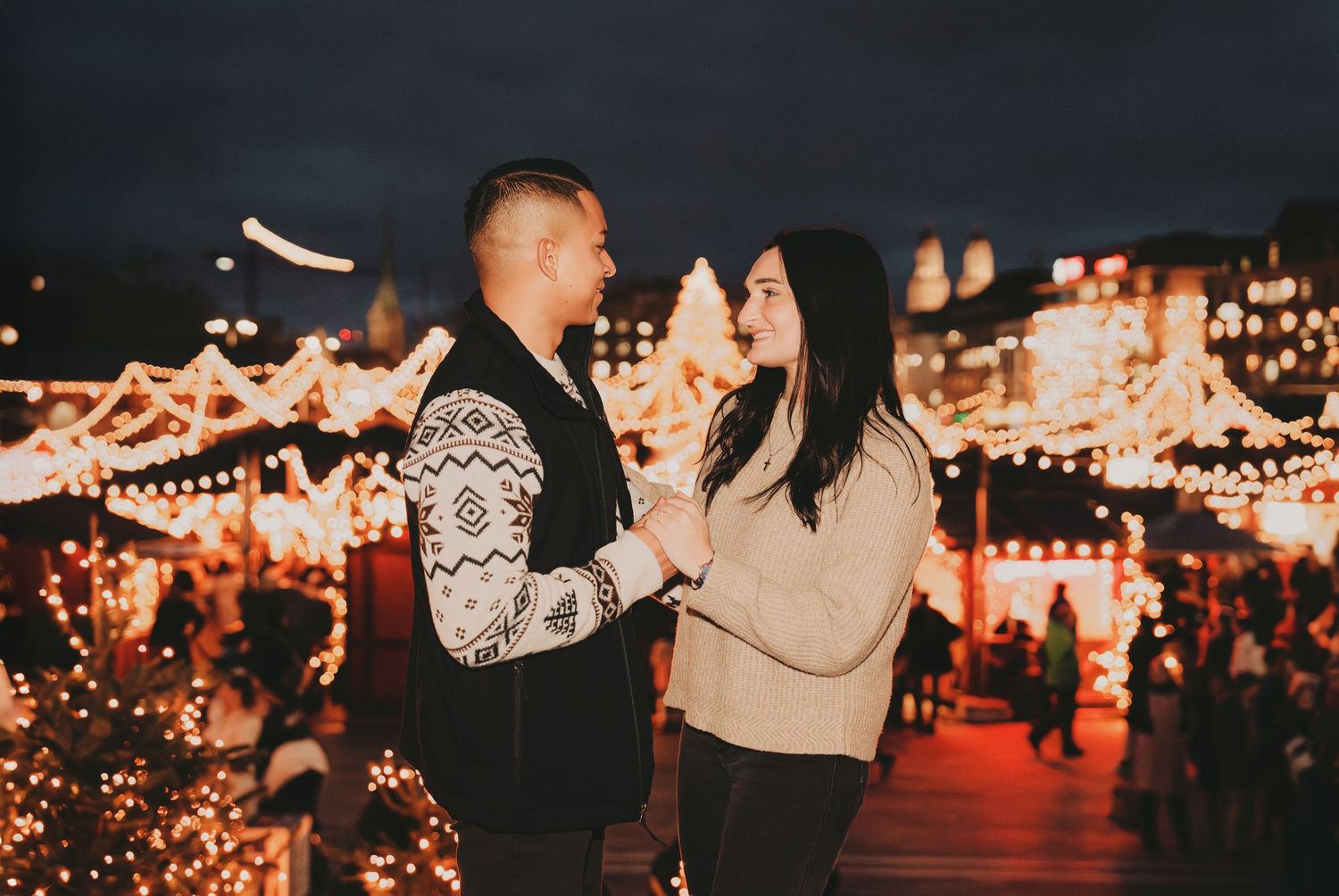 Romantic couple holding hands at a magical Christmas market with sparkling lights and festive stalls.