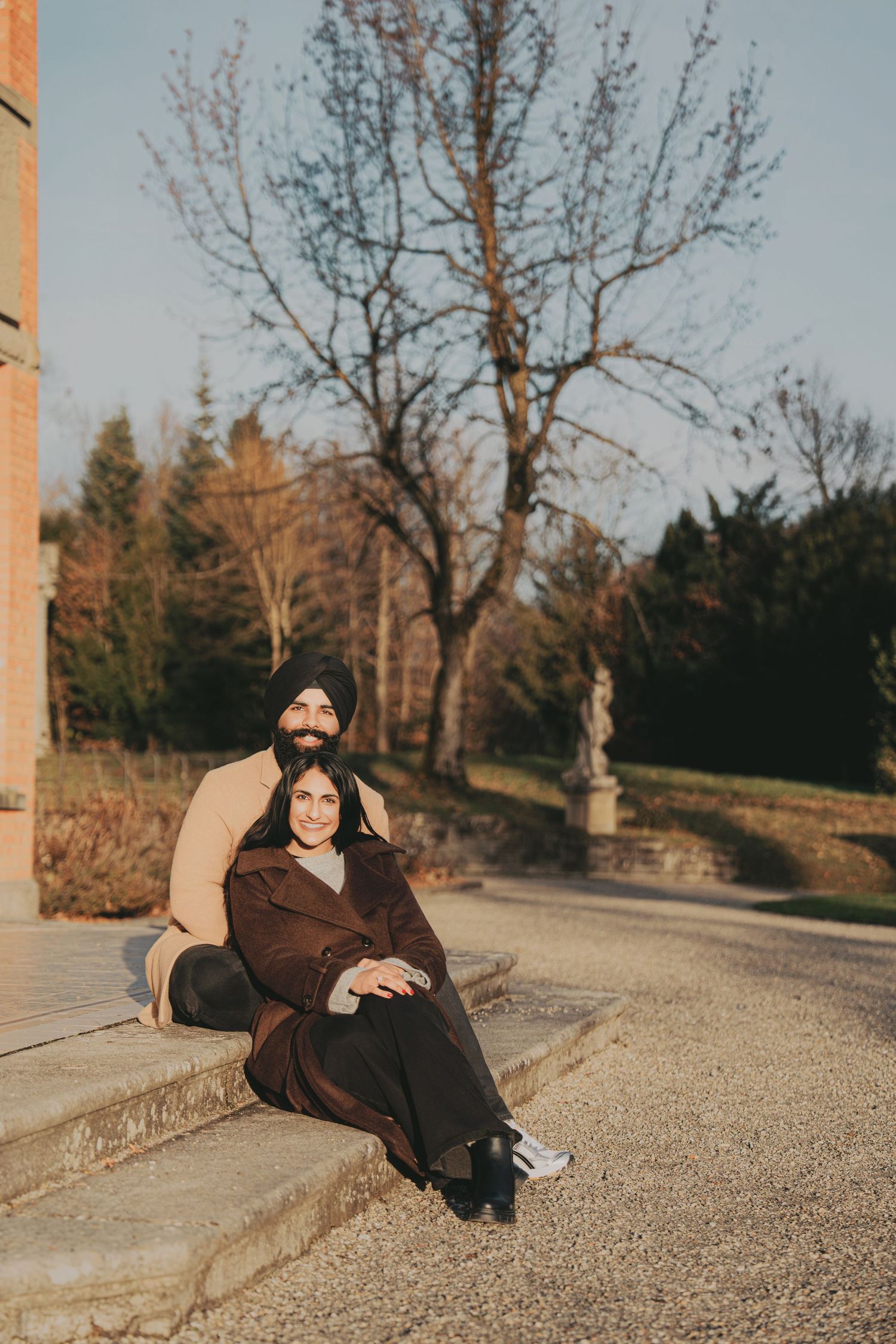 South Asian couple sitting together on steps in golden hour light surrounded by autumn trees.