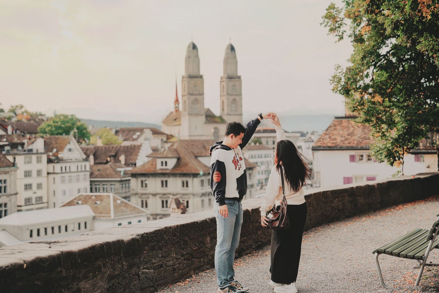 A couple shares a playful moment on a scenic Zurich overlook with rooftops and church towers behind them.