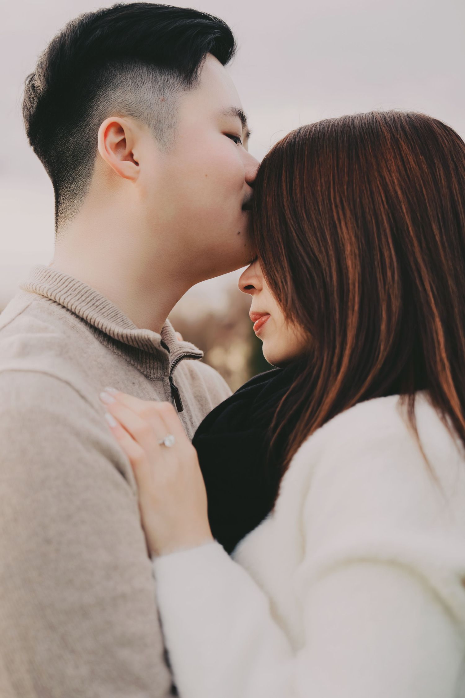 Close-up of couple sharing a tender forehead kiss outdoors, woman wearing an engagement ring.