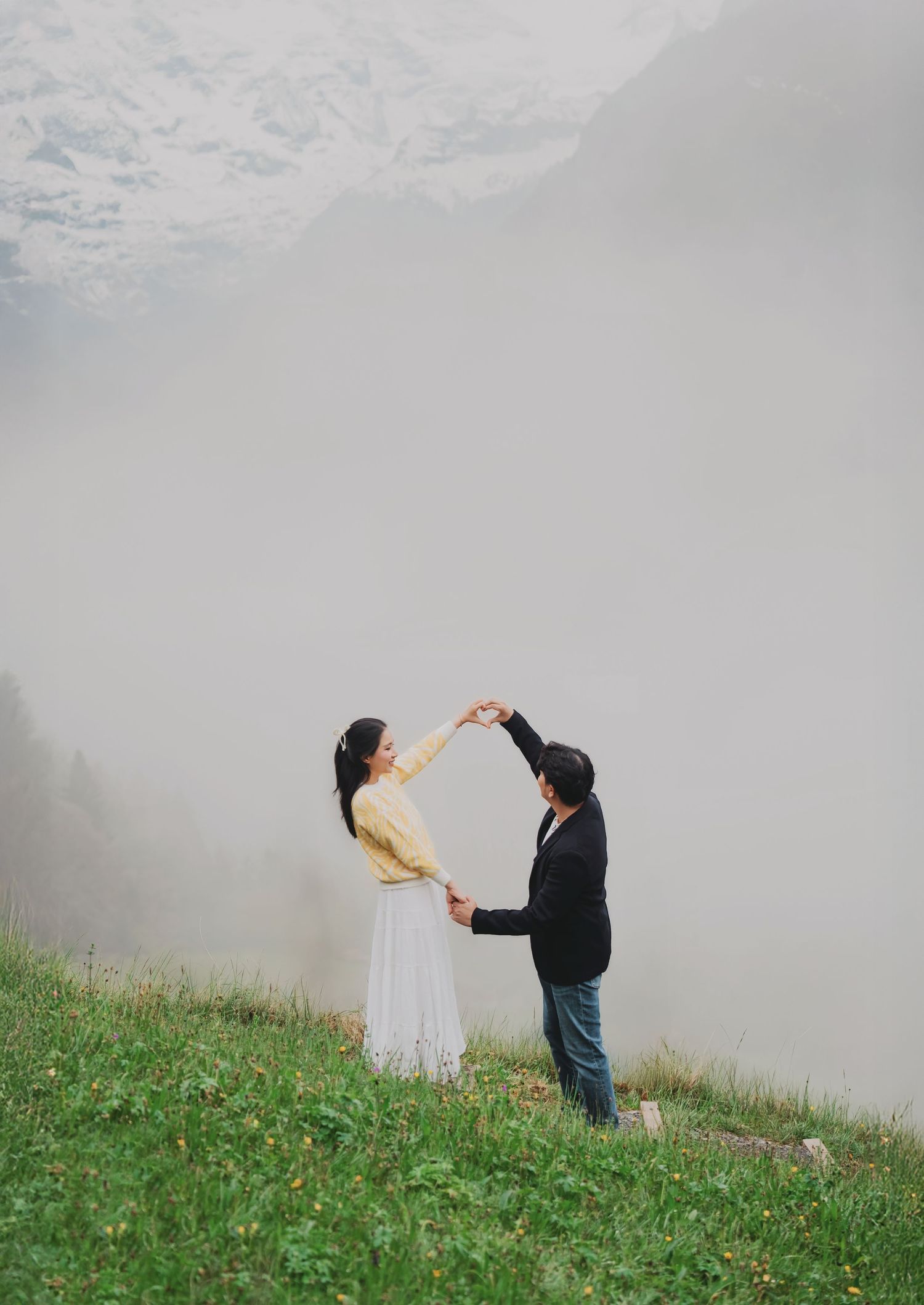 Couple dancing together on a foggy green hillside with misty mountains in the background.
