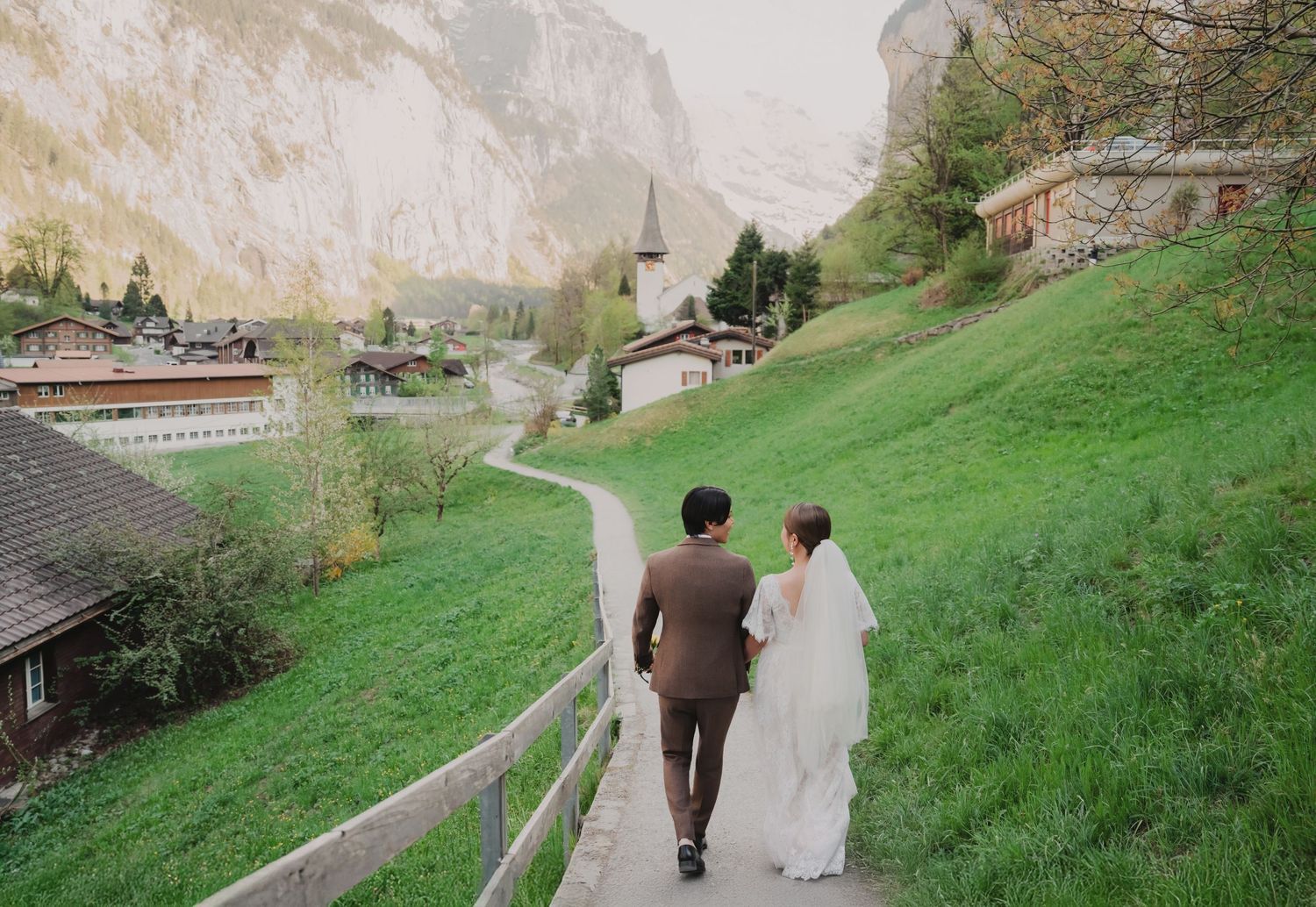 Couple in wedding attire walking hand in hand on a scenic path in Lauterbrunnen, Switzerland.