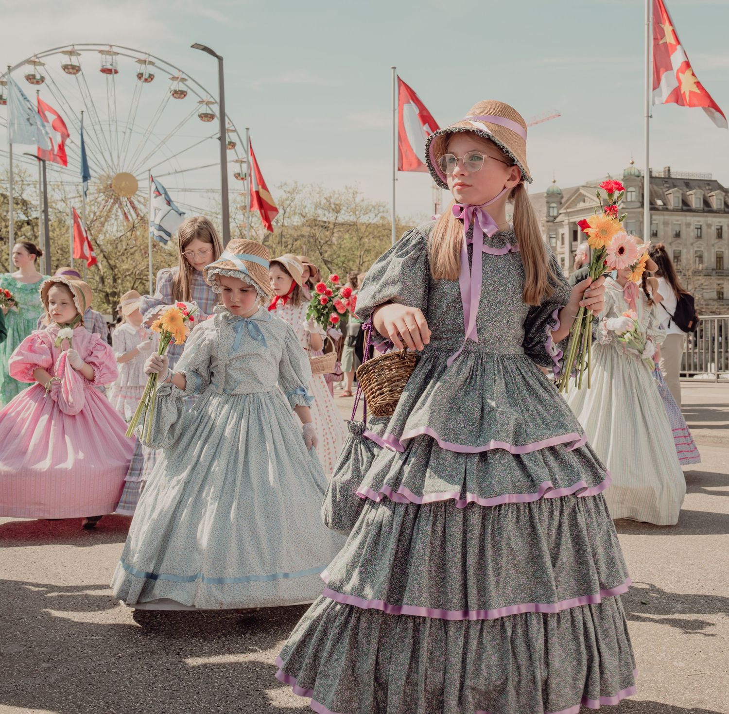 Girls in colorful vintage tiered dresses and bonnets carry flower baskets in festive spring parade.