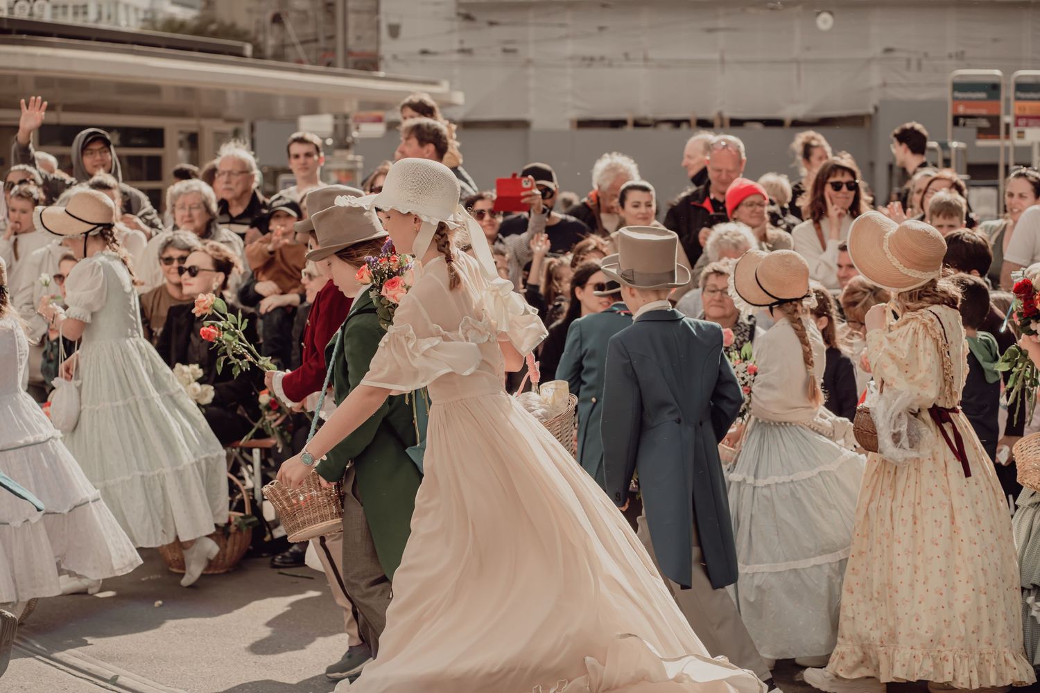 People in Victorian-era white dresses and period costumes dancing together during an outdoor street festival parade.