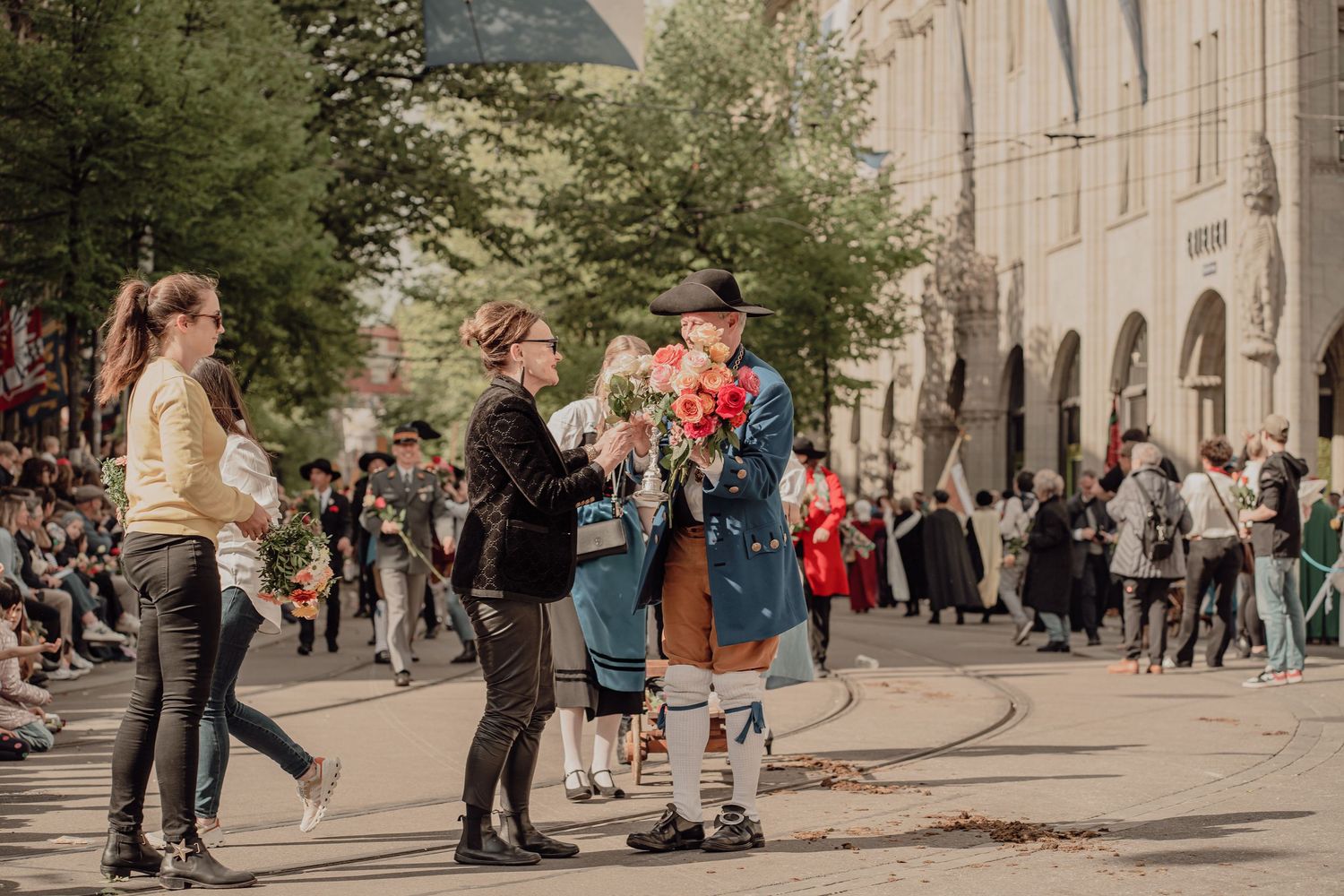 A man in historic Bavarian costume presents red roses to spectators during a traditional street parade.