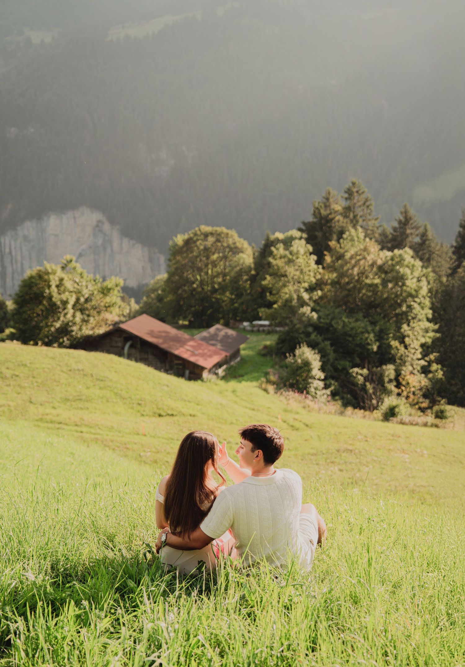 Couple sitting together on sunny Swiss alpine hillside gazing at stunning mountain valley view.
