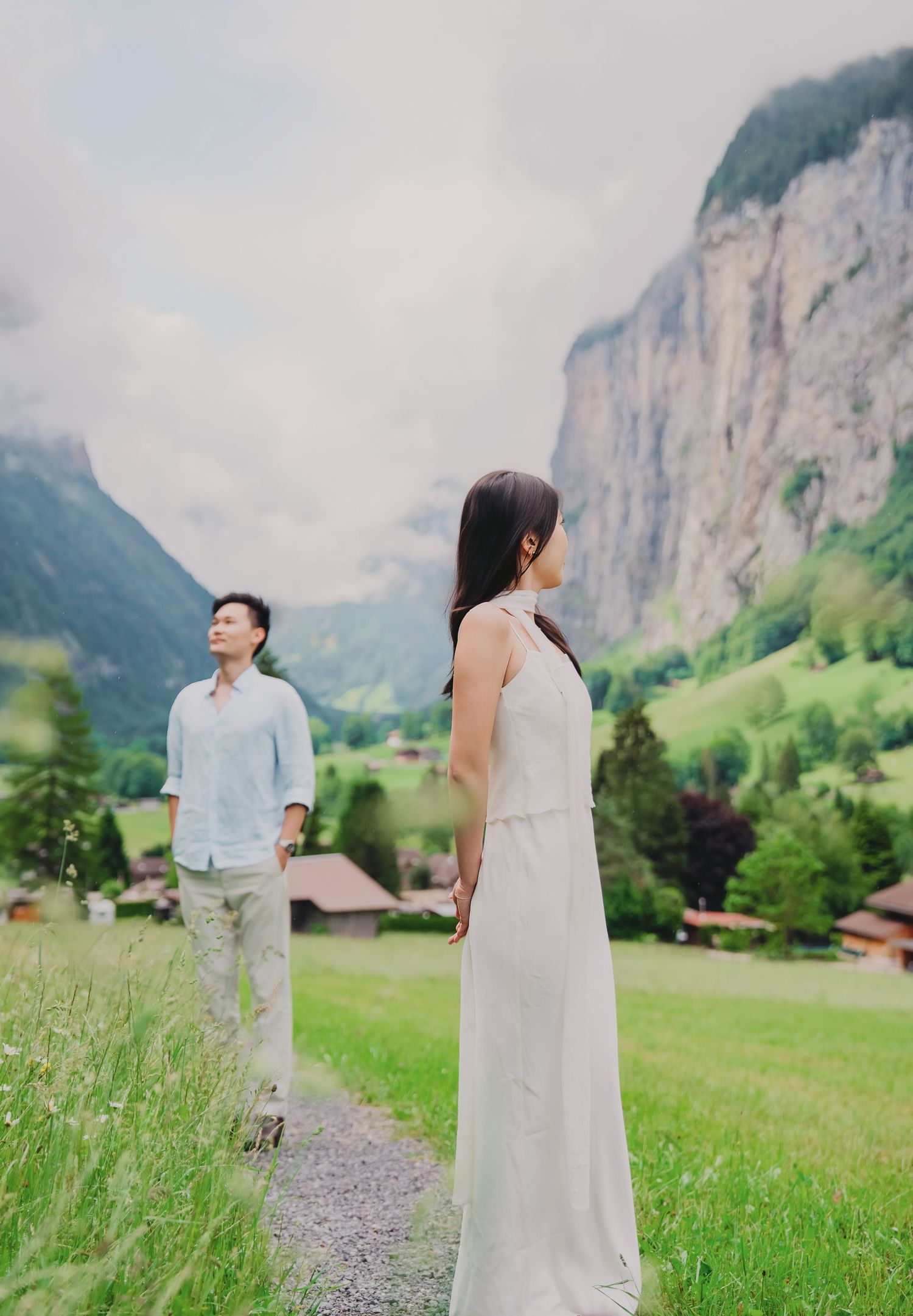 Couple in white dress and blue shirt holding hands on a mountain valley path in Lauterbrunnen, Switzerland.