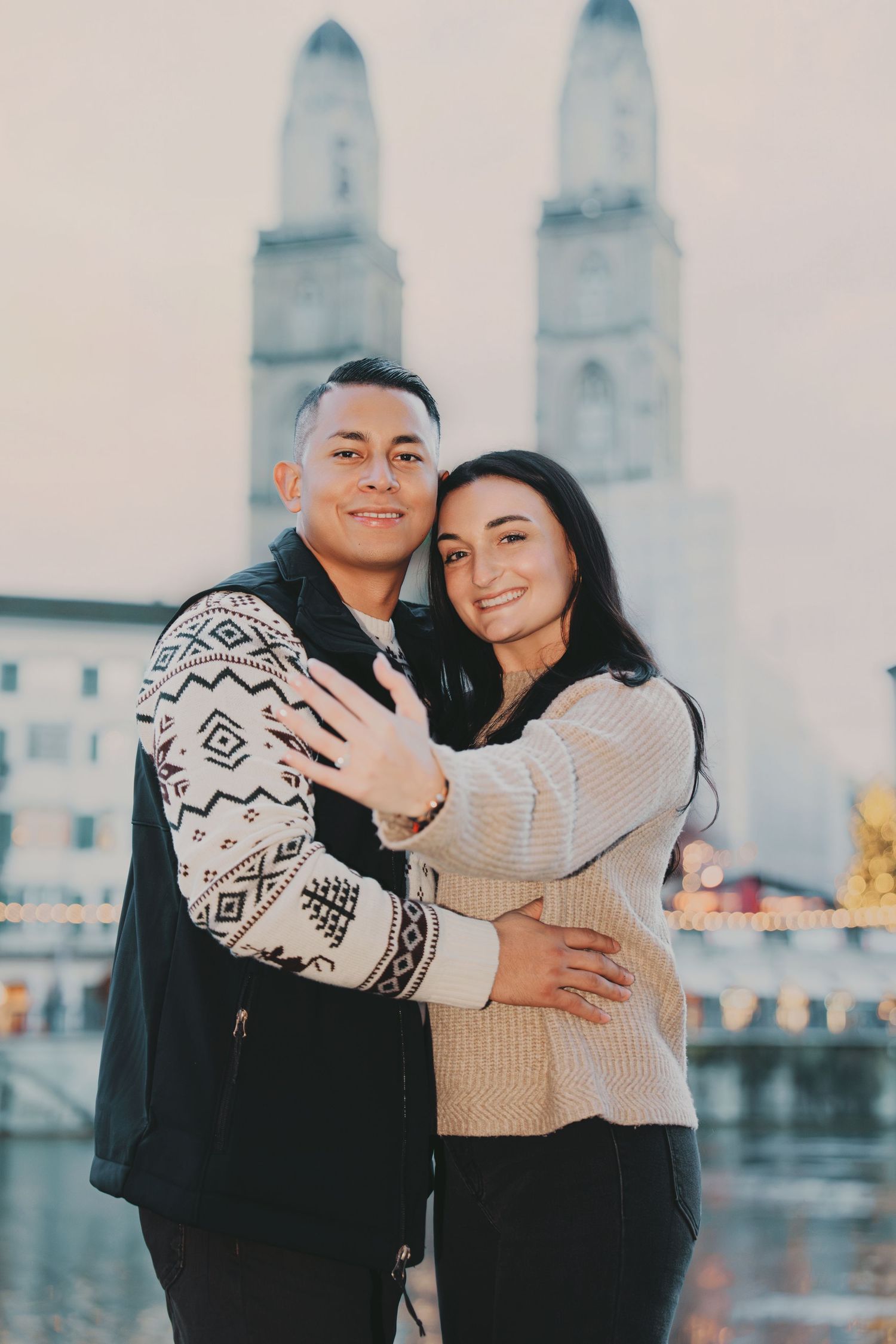 Smiling couple hugging closely with Grossmünster church and river in background in Zurich.