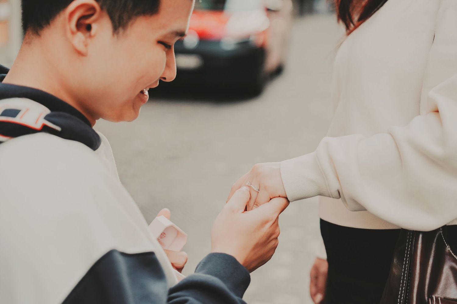 Close-up of man placing engagement ring on womans finger during street proposal.