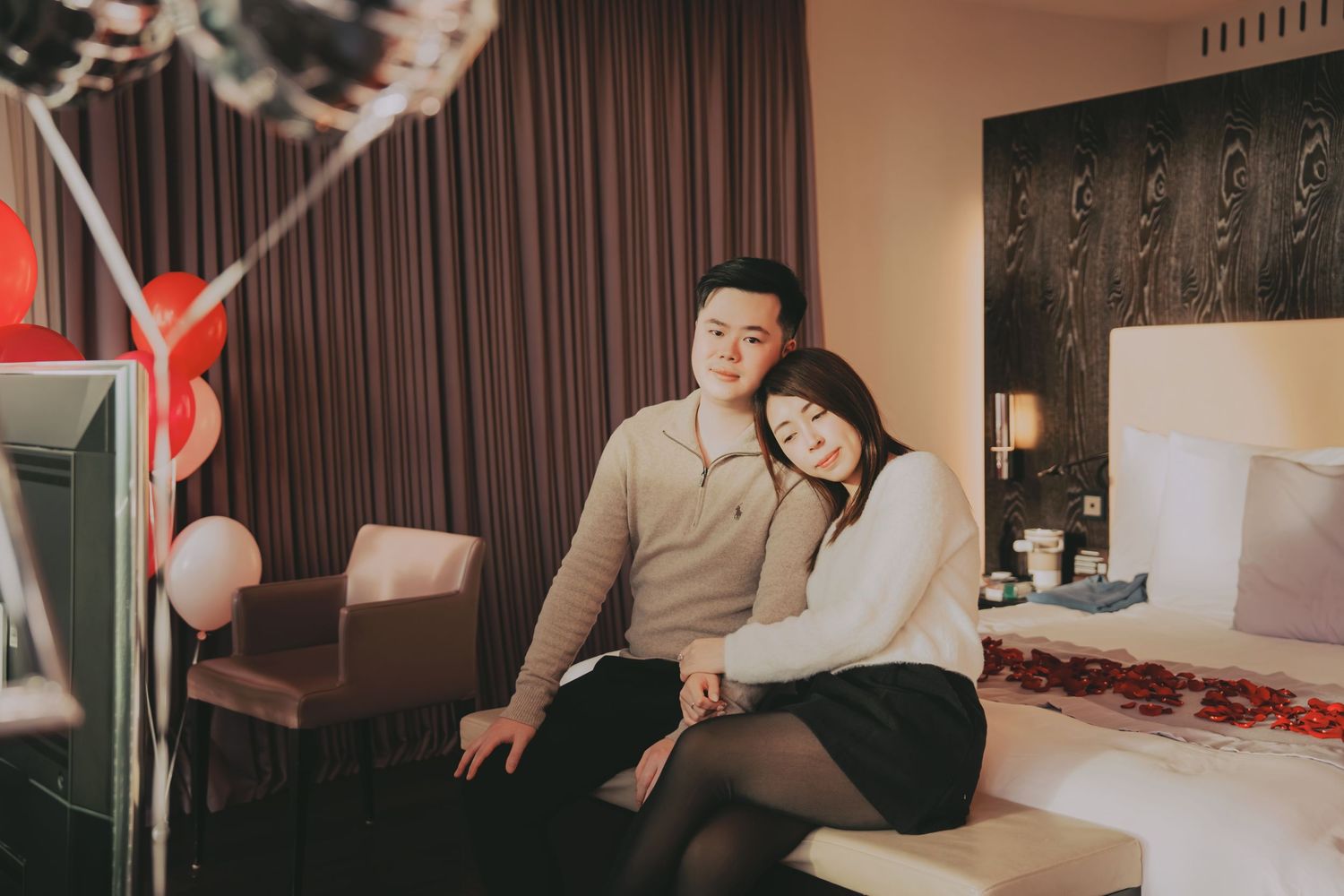 Couple sitting together in romantic hotel room decorated with heart balloons.