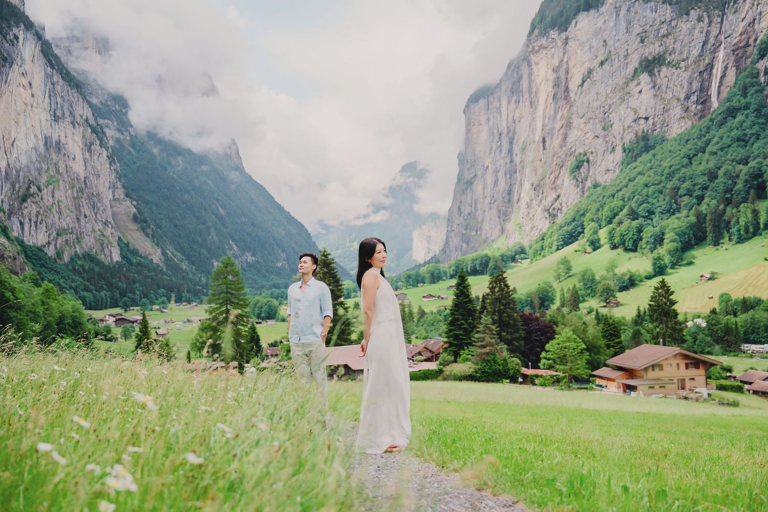 Couple in wedding attire holding hands in lush Lauterbrunnen valley Switzerland with dramatic cliffs and alpine village backdrop.