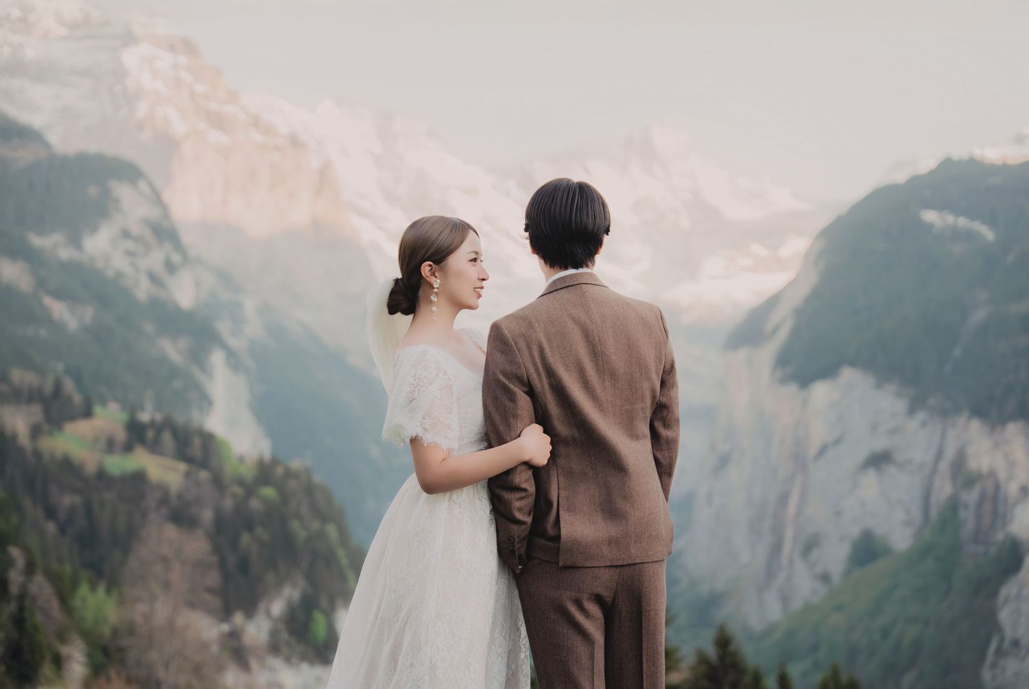 Elegant bride and groom standing close together overlooking a dramatic Swiss alpine valley and mountain scenery.