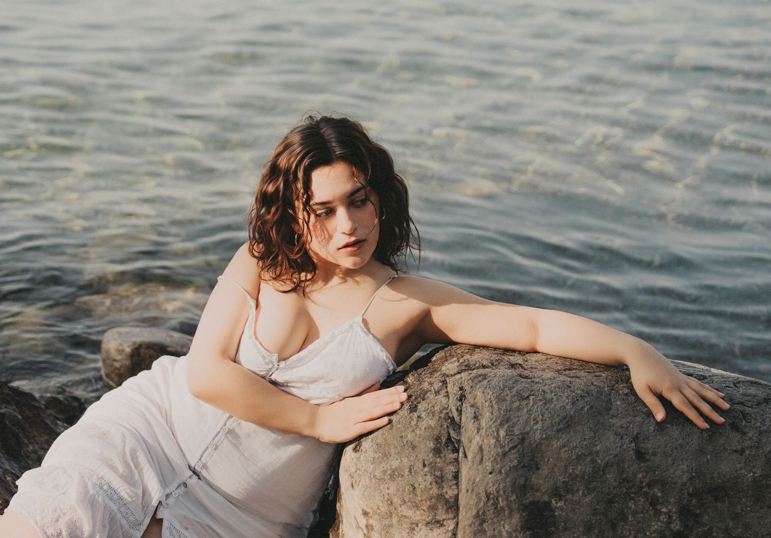 Young woman in white dress leaning on a rock near the sea.