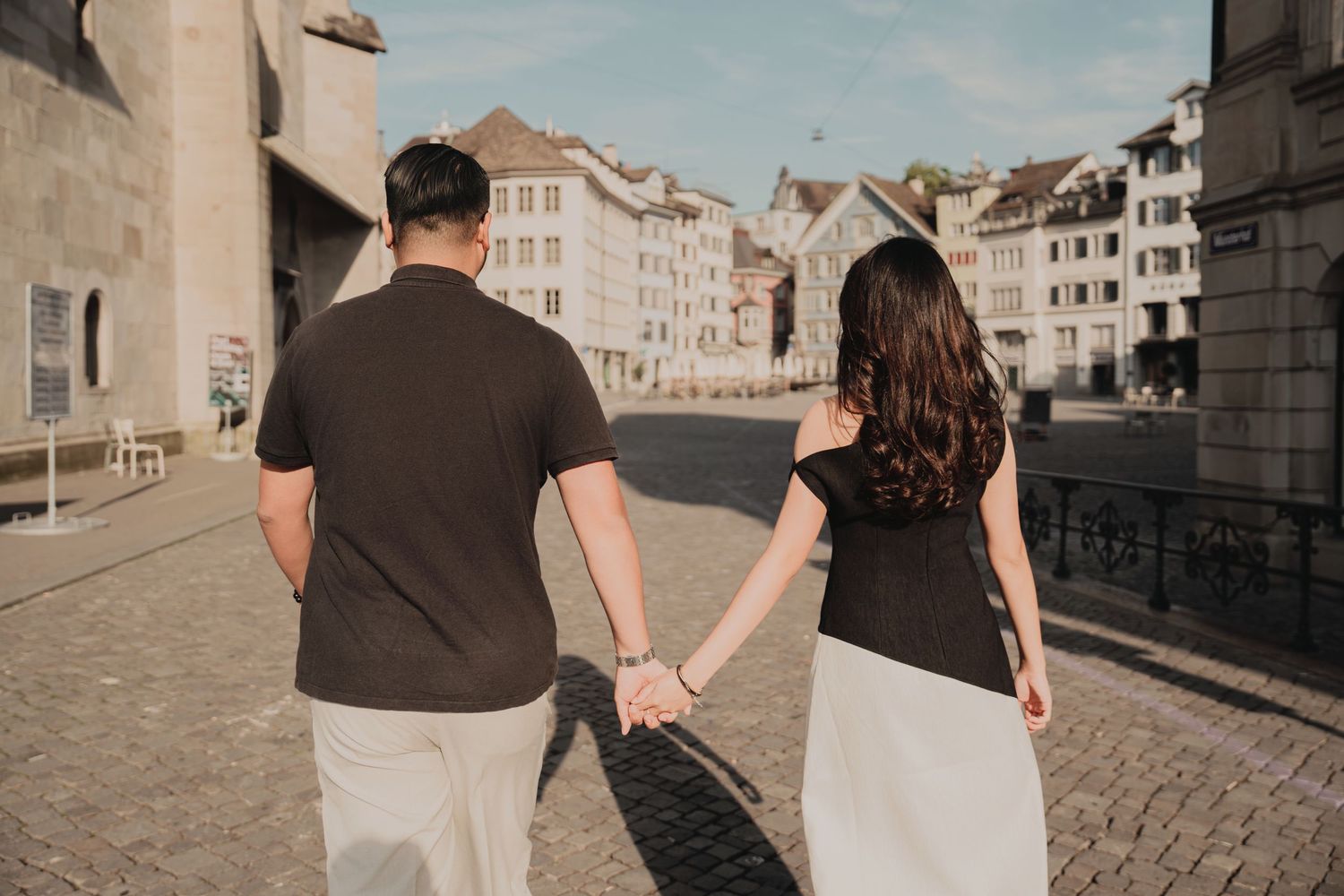 Couple walking hand in hand through sunny cobblestone square in Zurich old town.