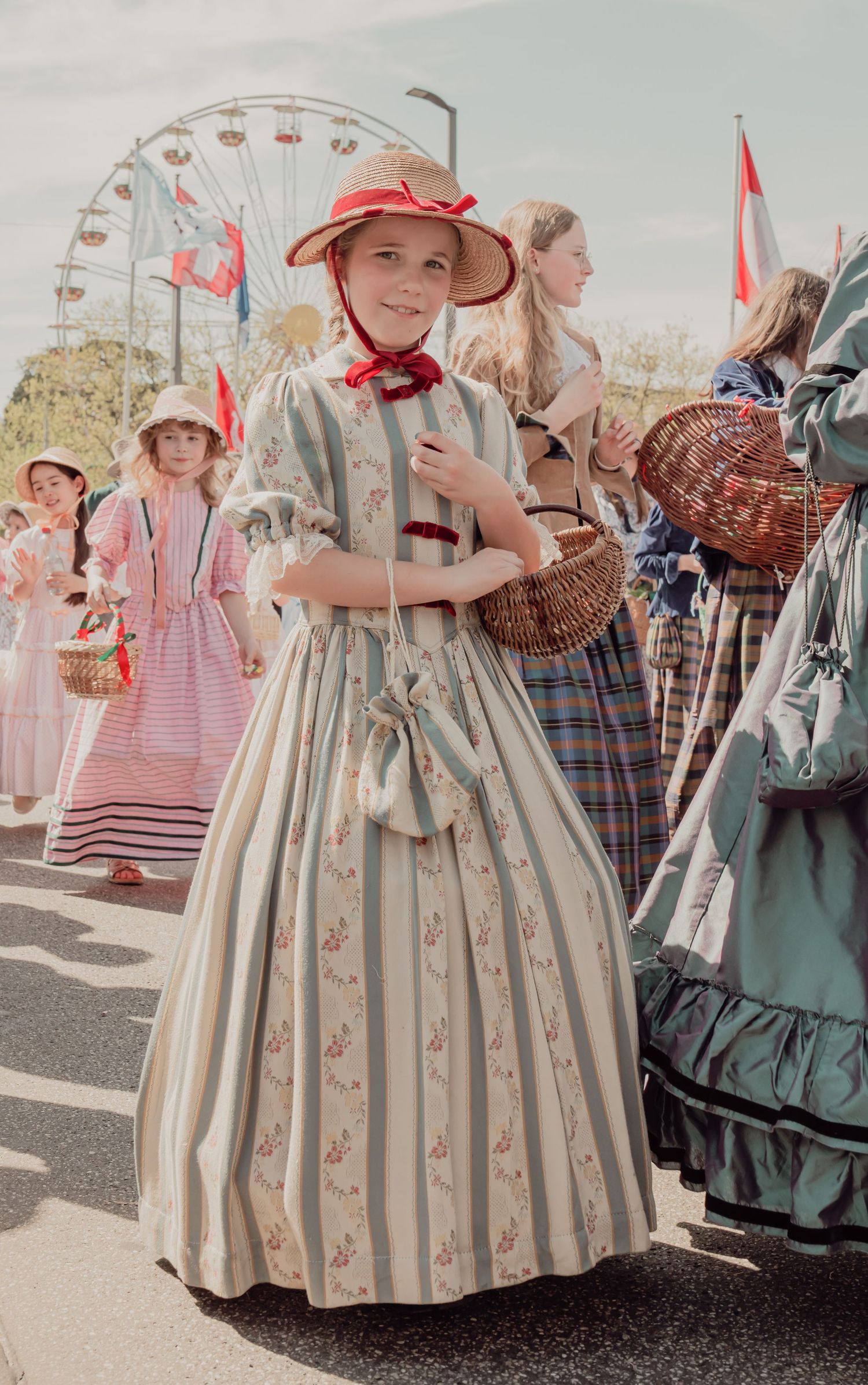 Young girl in vintage Victorian floral dress and red hat at a historical costume parade.