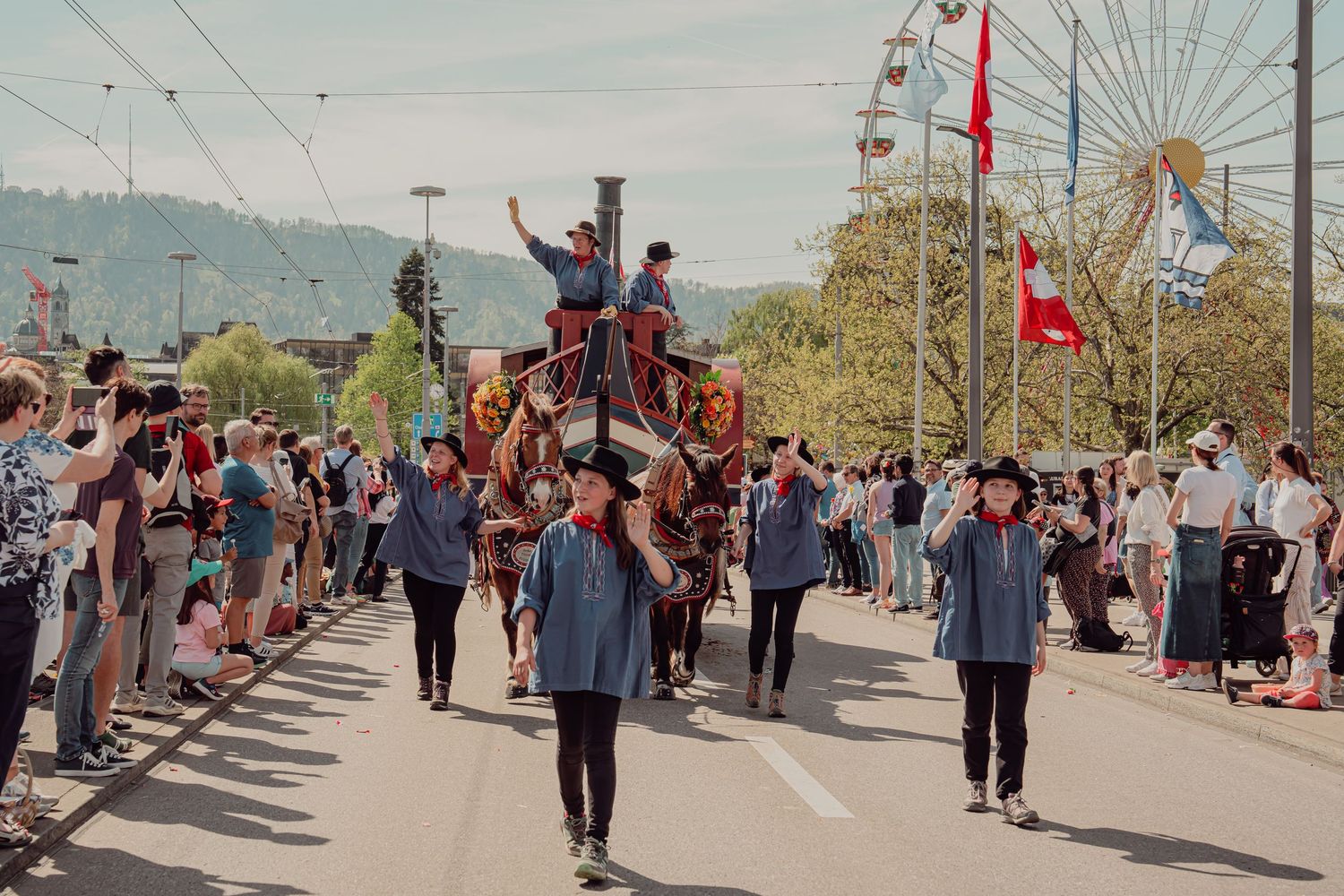 Horse-drawn carriage with riders waves to crowds at a lively outdoor festival parade.