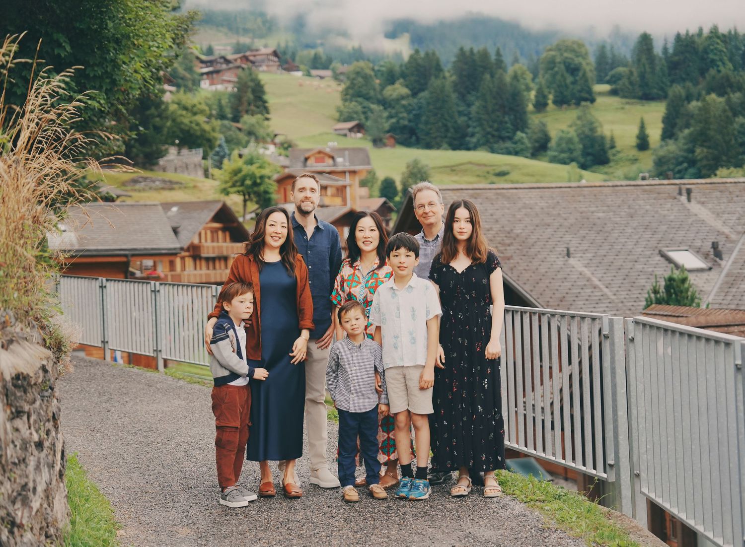 A multigenerational family poses together on a path with a misty Swiss alpine village backdrop.