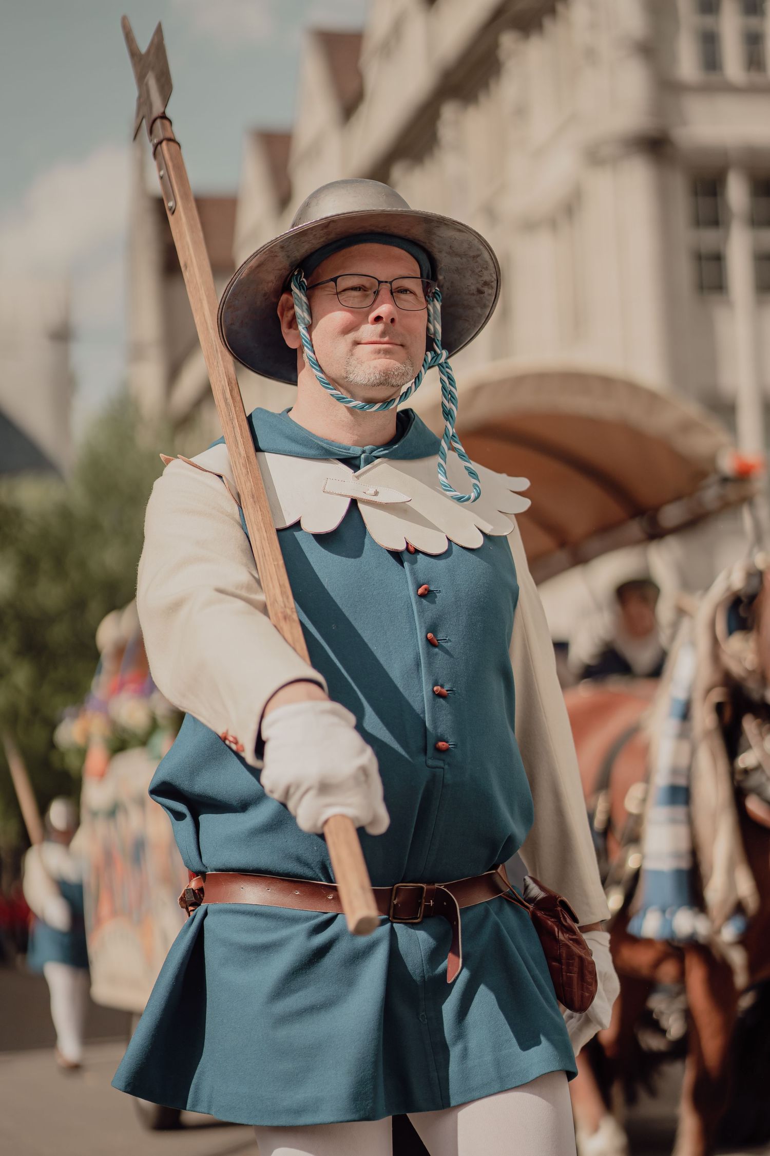 Man in medieval blue and white costume carries a spear during a historical street parade.