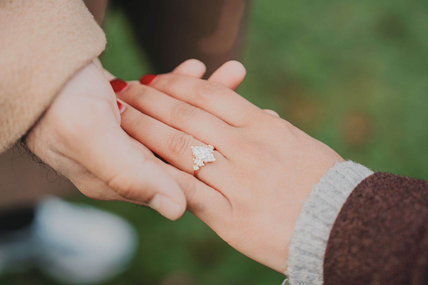 Close-up of an engagement ring with a halo diamond setting on a womans hand held by her partner.