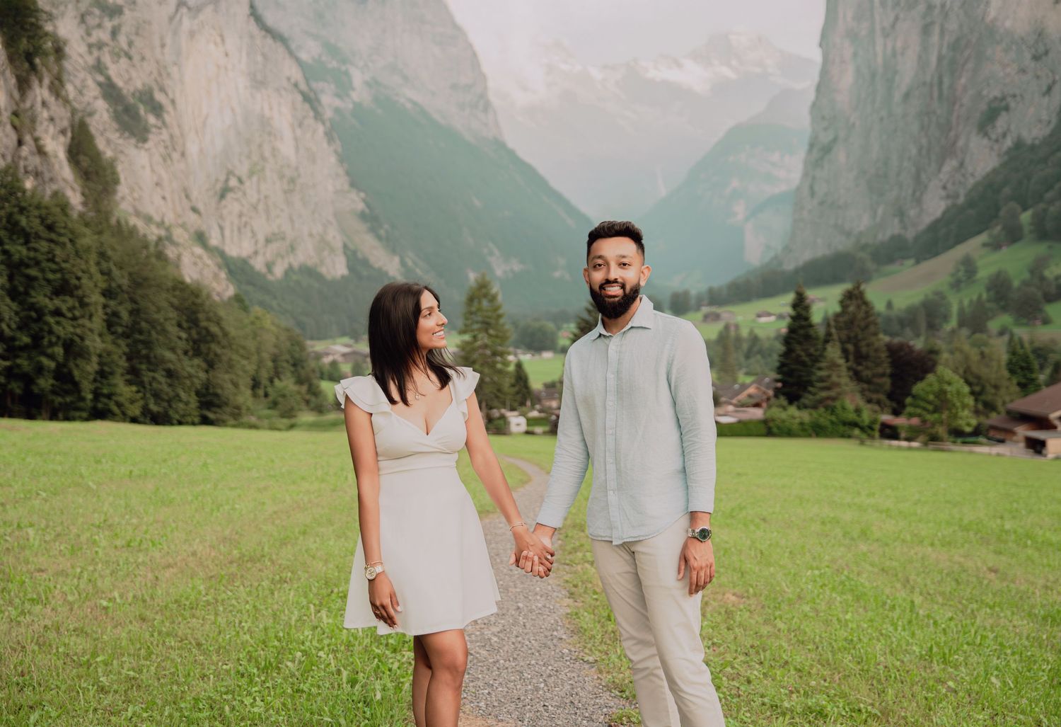 Engaged couple holding hands in a scenic Swiss alpine valley with mountains in the background.