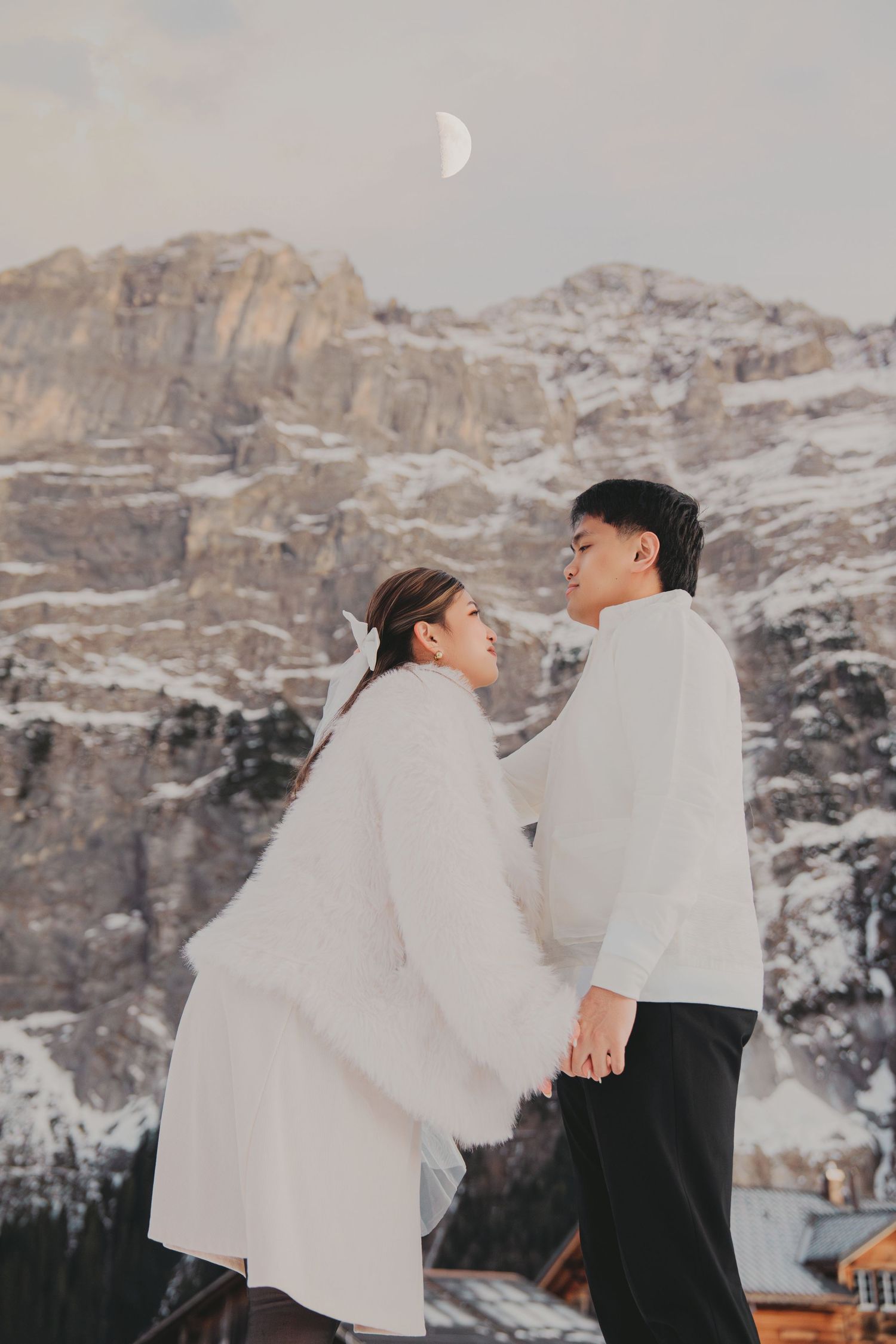 Romantic couple holding hands and gazing at each other with snowy mountain and crescent moon behind.