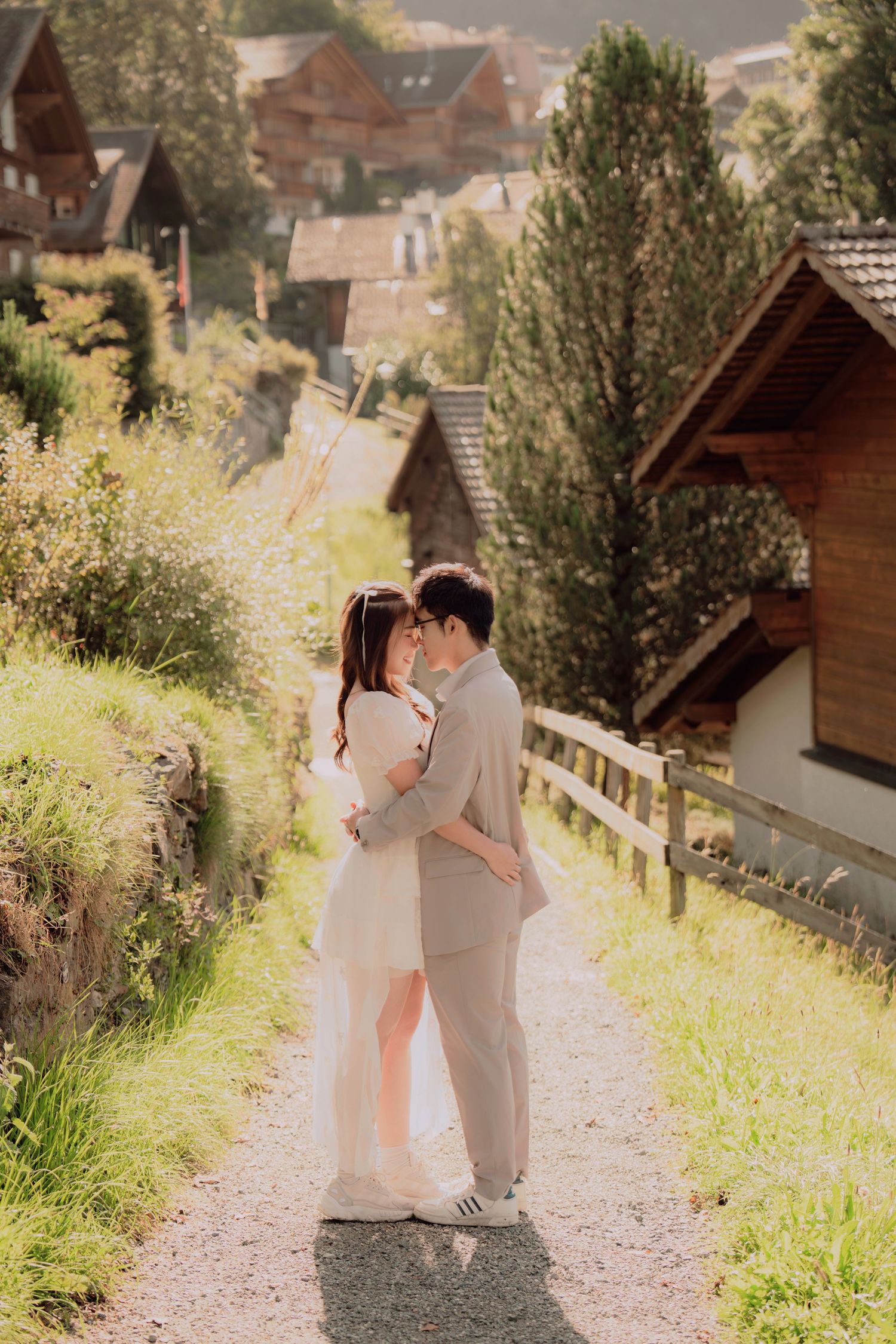 Couple sharing a romantic kiss on a gravel path surrounded by wildflowers and Swiss chalet village.
