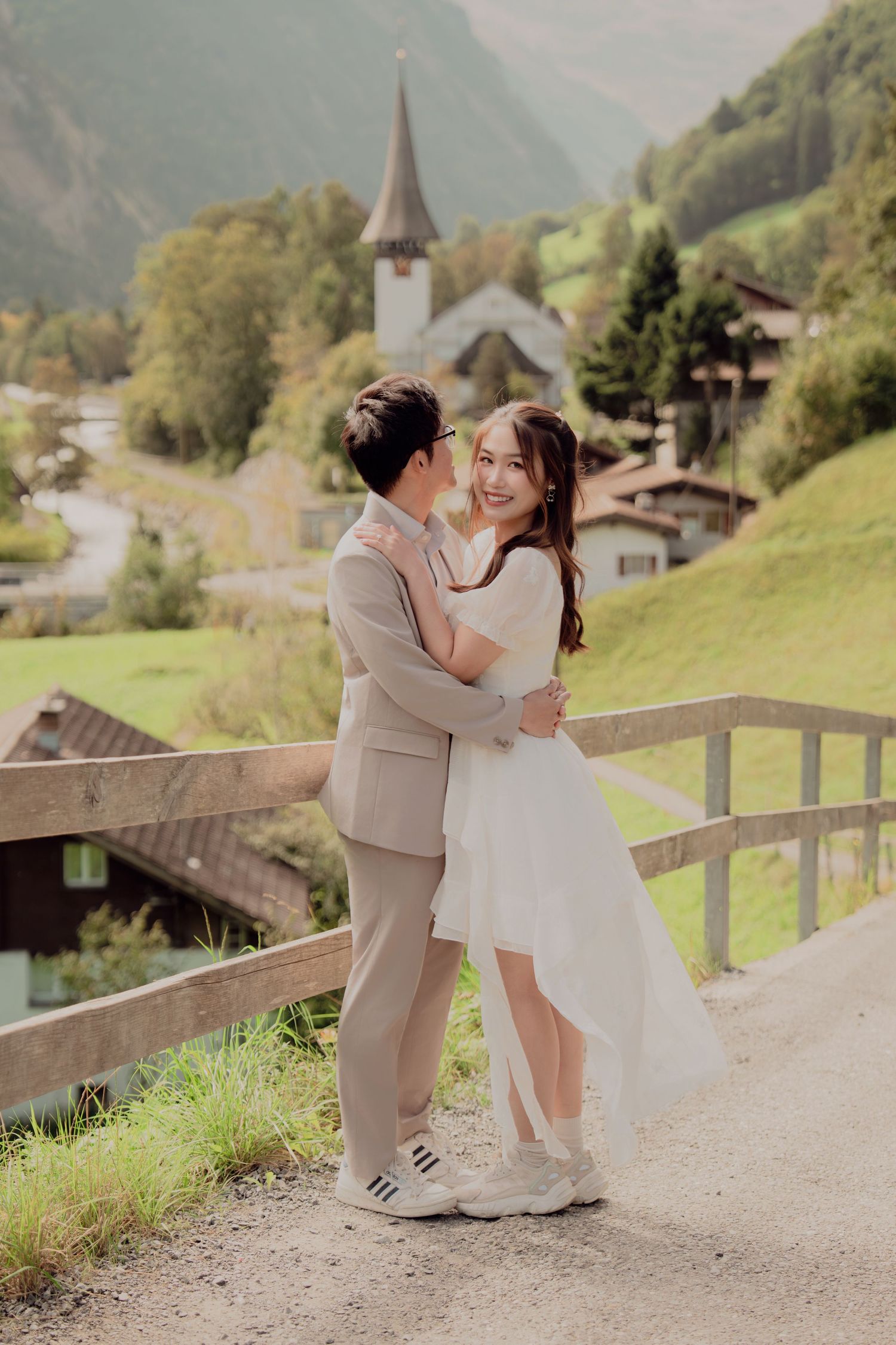 Laughing bride and groom embracing on a scenic path with Lauterbrunnen Swiss village in background.