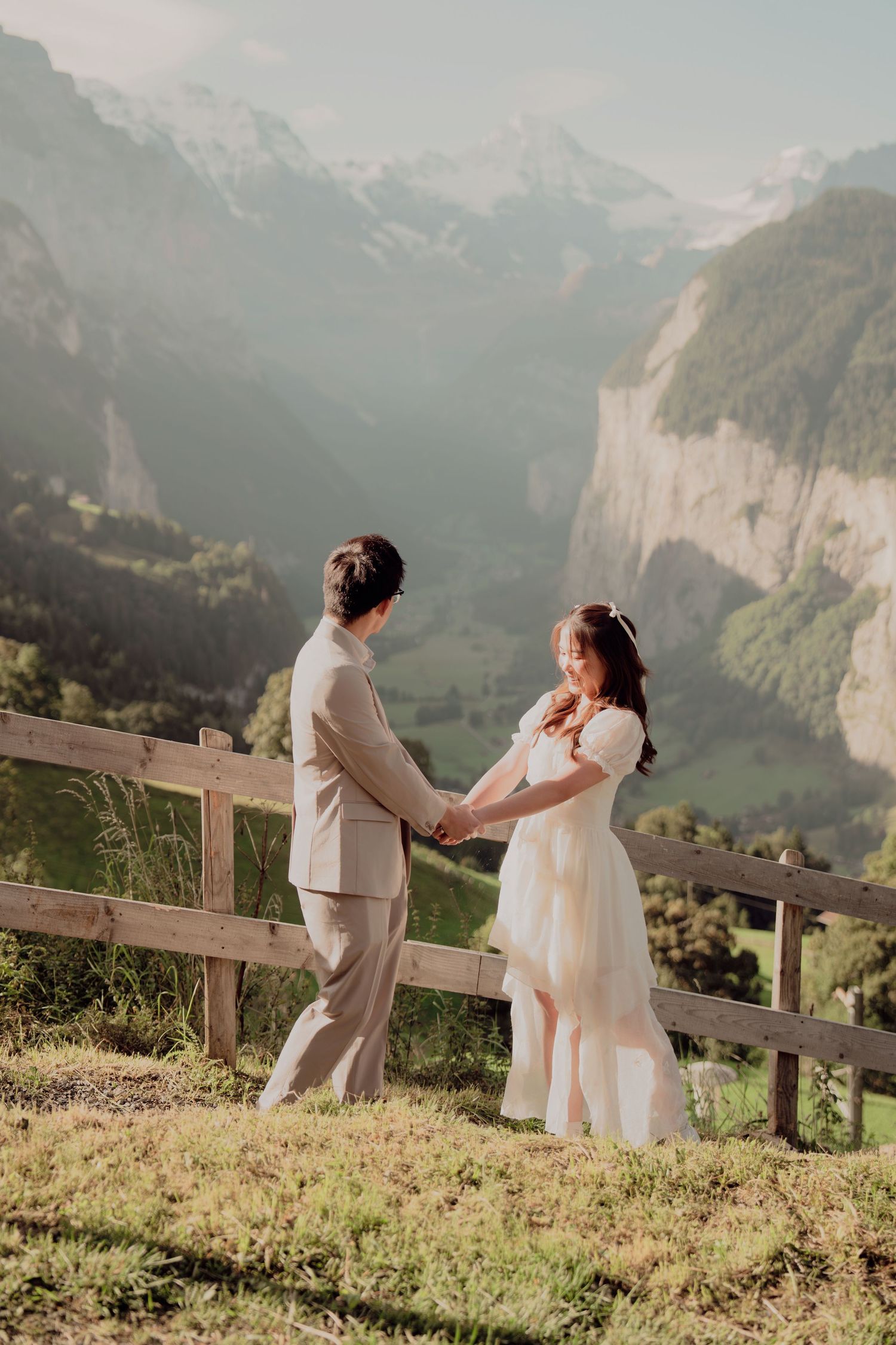 Bride and groom holding hands facing each other with stunning Swiss mountain cliffs in the background.