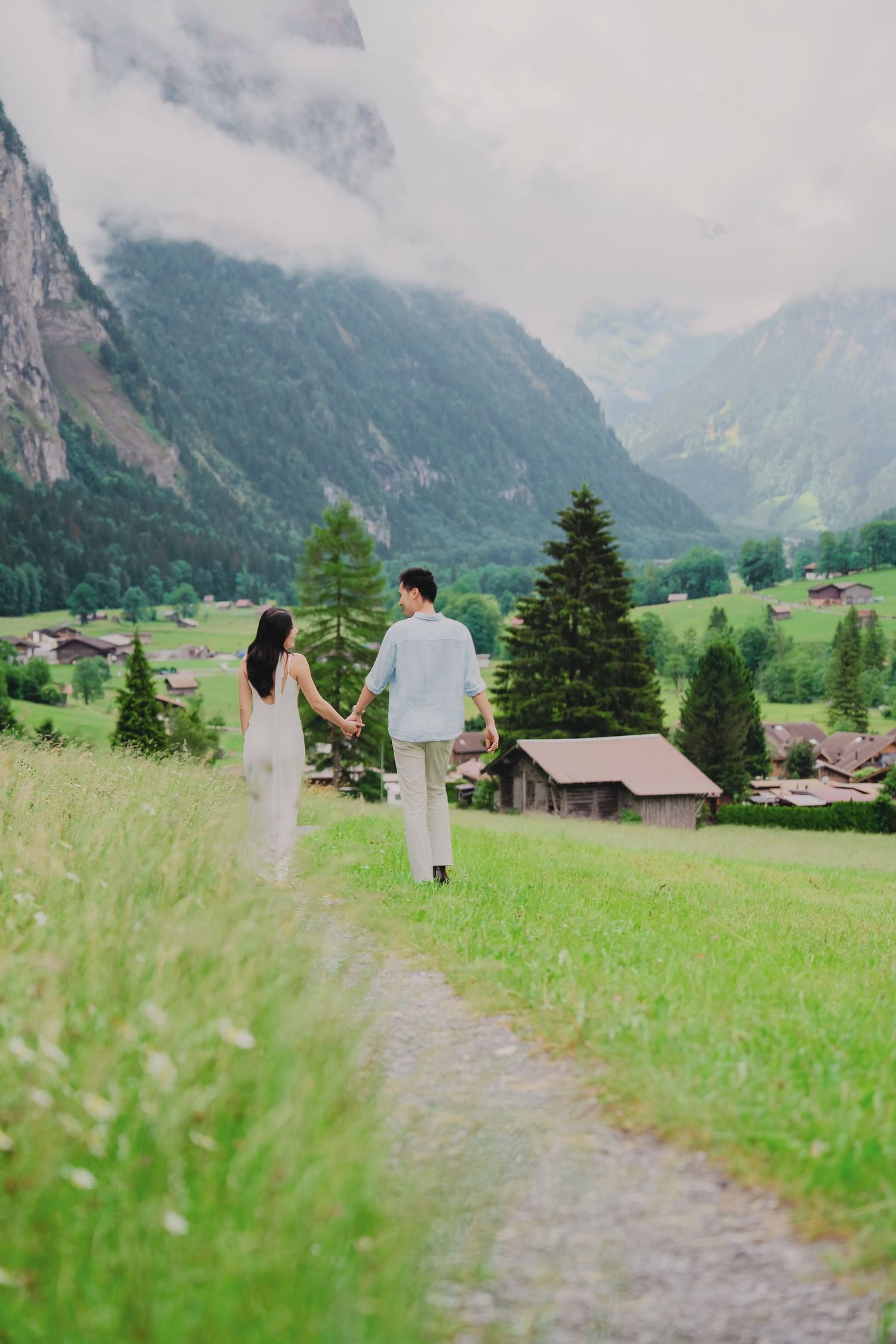 Couple walking hand in hand along a grassy path with Alpine village and mountain scenery in Lauterbrunnen.