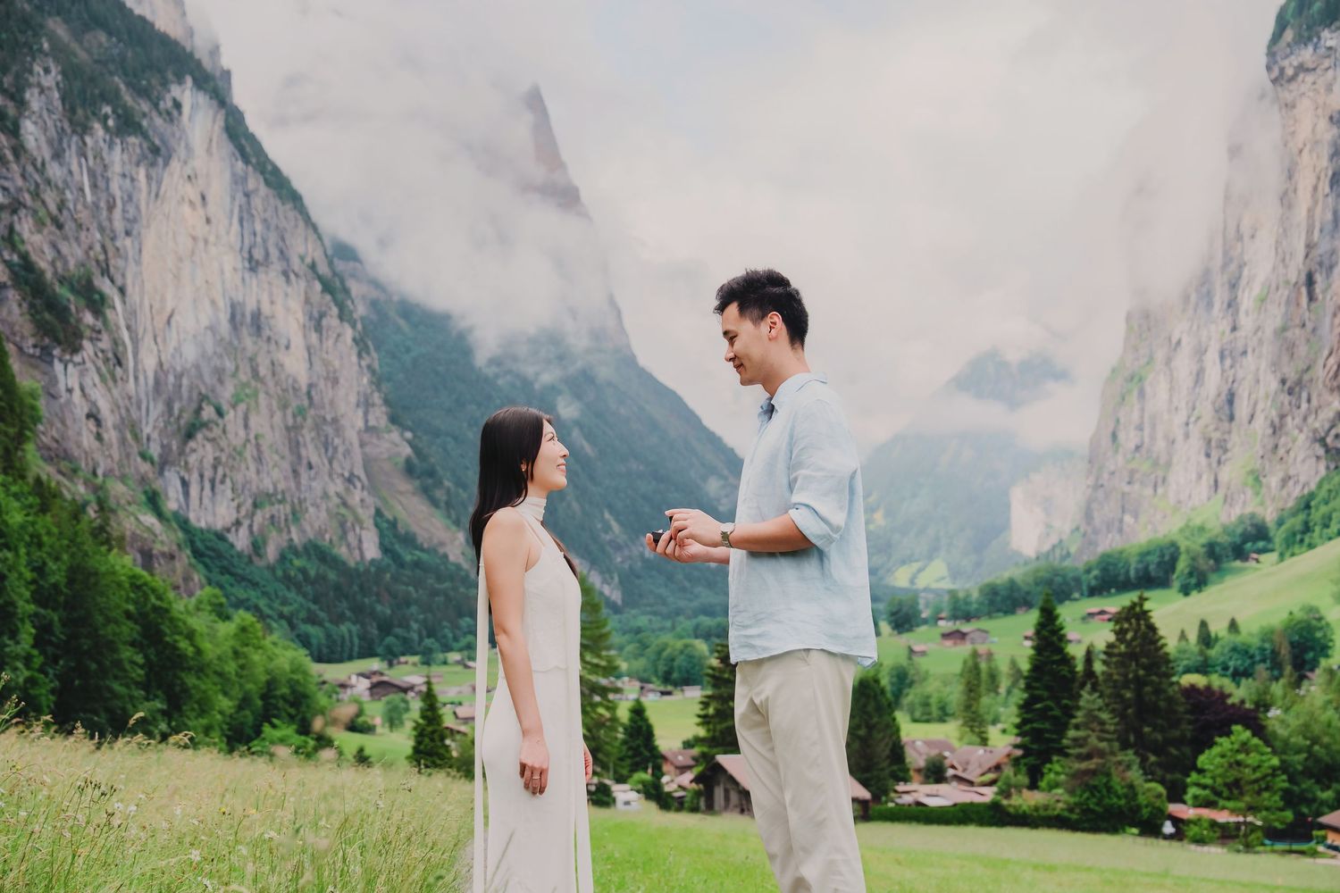 Couple standing in a lush green valley with dramatic mountain cliffs and clouds in Lauterbrunnen, Switzerland.