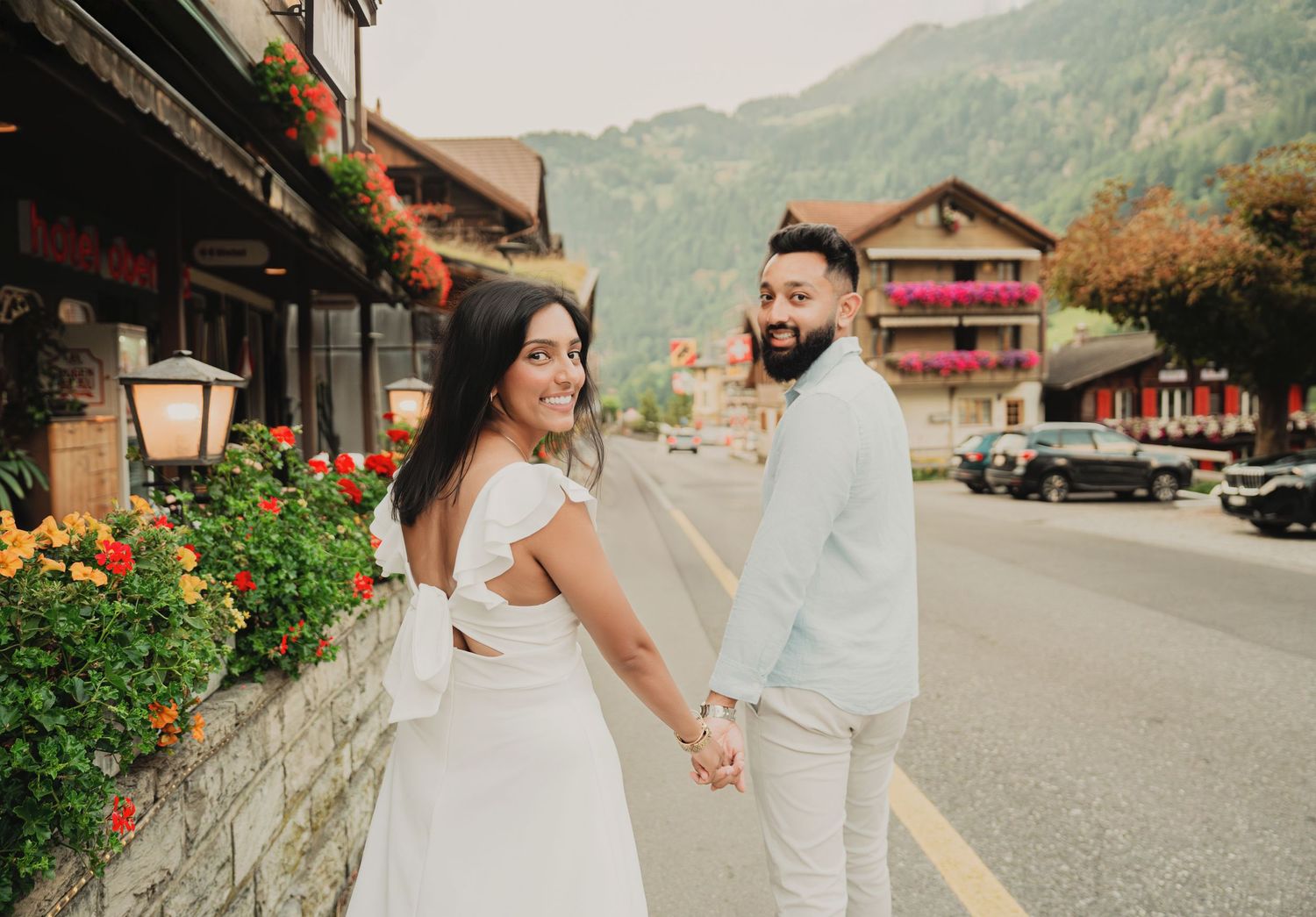 Couple holding hands on a flower-lined street in a charming Swiss alpine village.